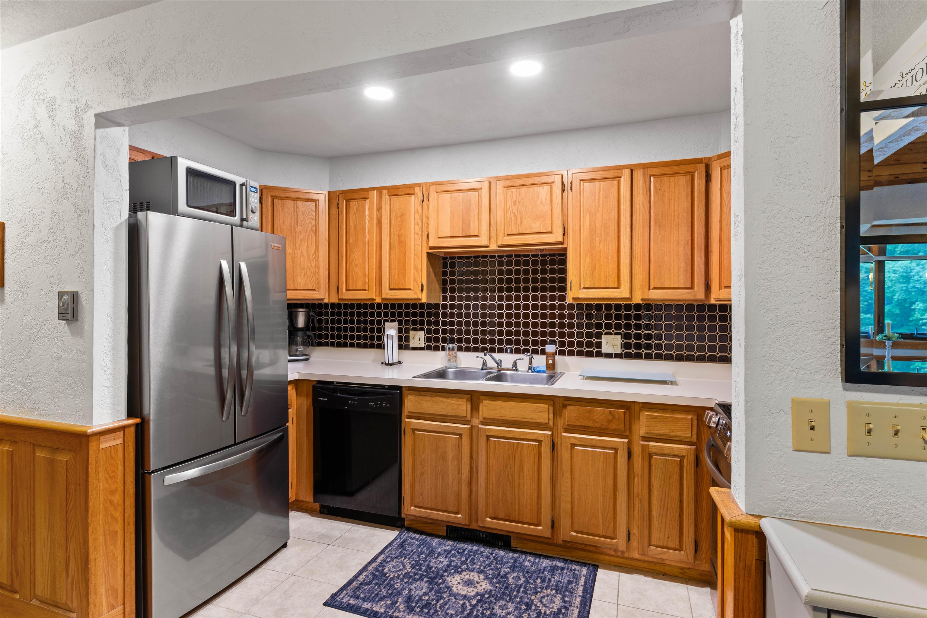 Kitchen with wood cabinets, dark geometric tile backsplash, and stainless-steel refrigerator.