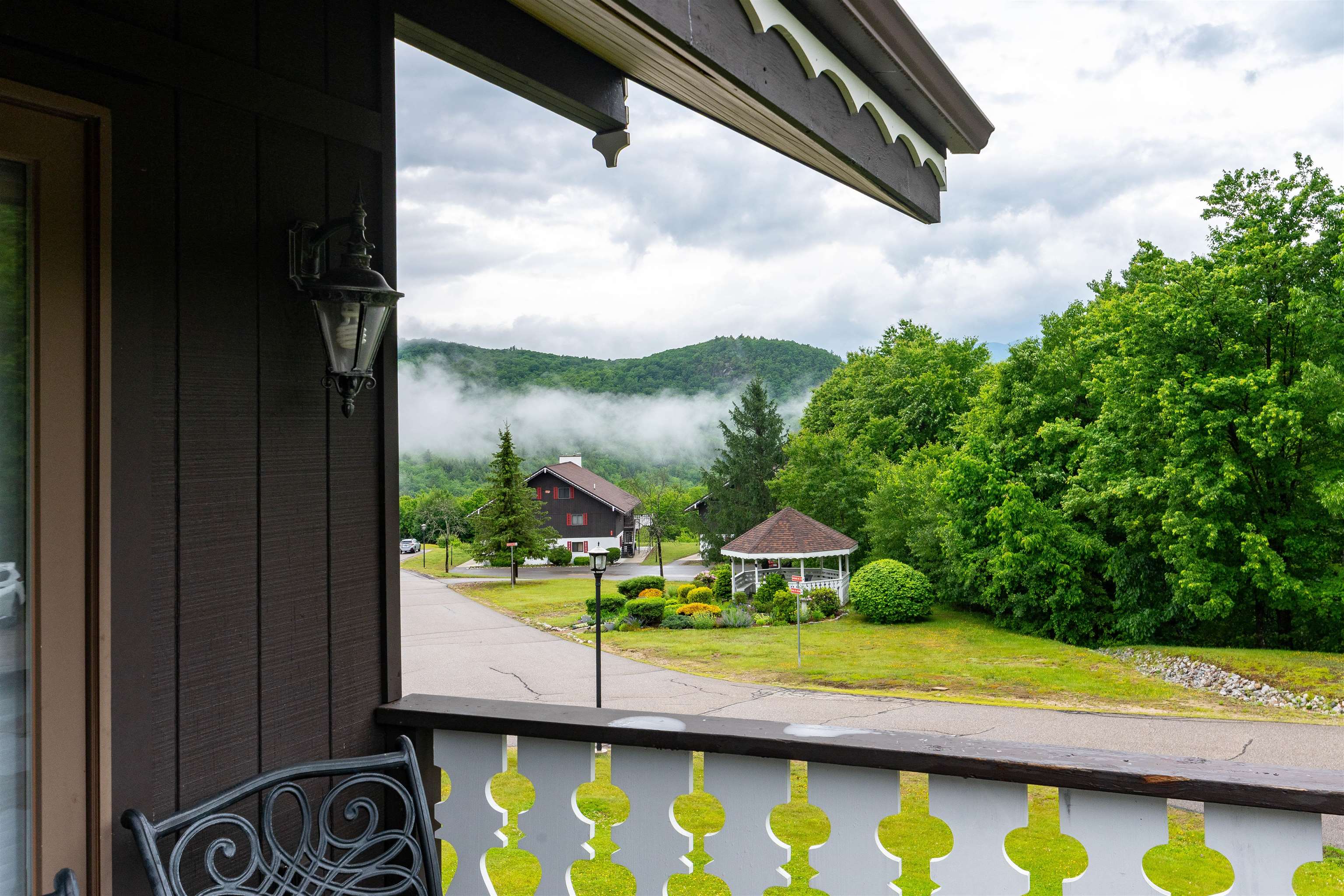 Covered porch overlooking a gazebo, neighboring building, and misty green hills.