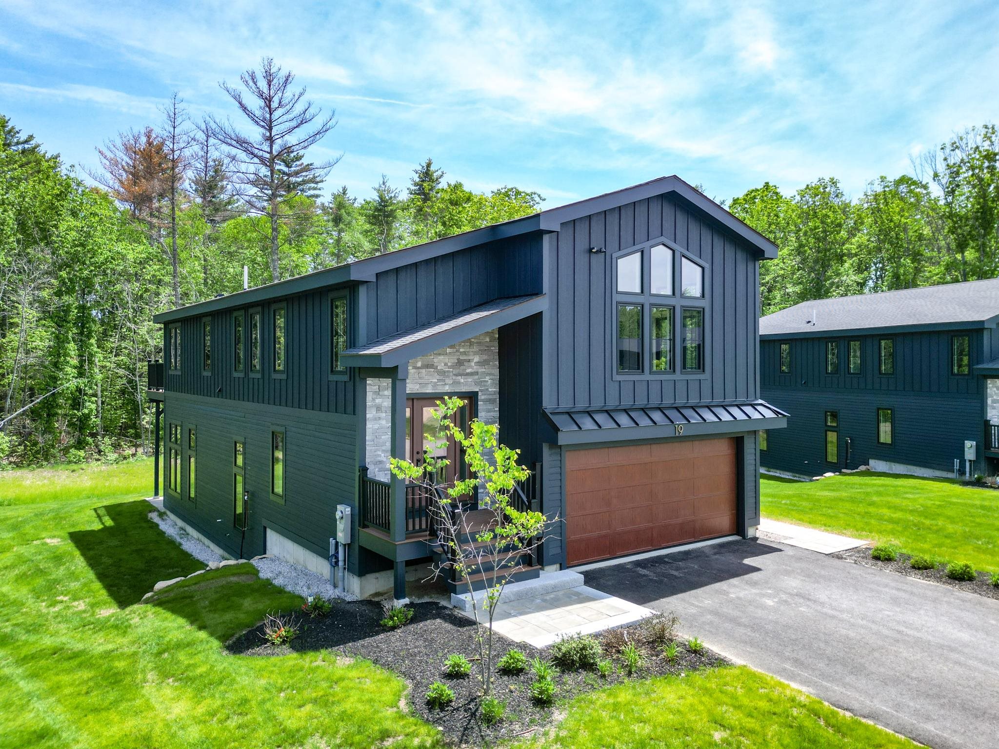 Modern dark-sided home with a stone entry, tall gabled windows, and brown double garage door.