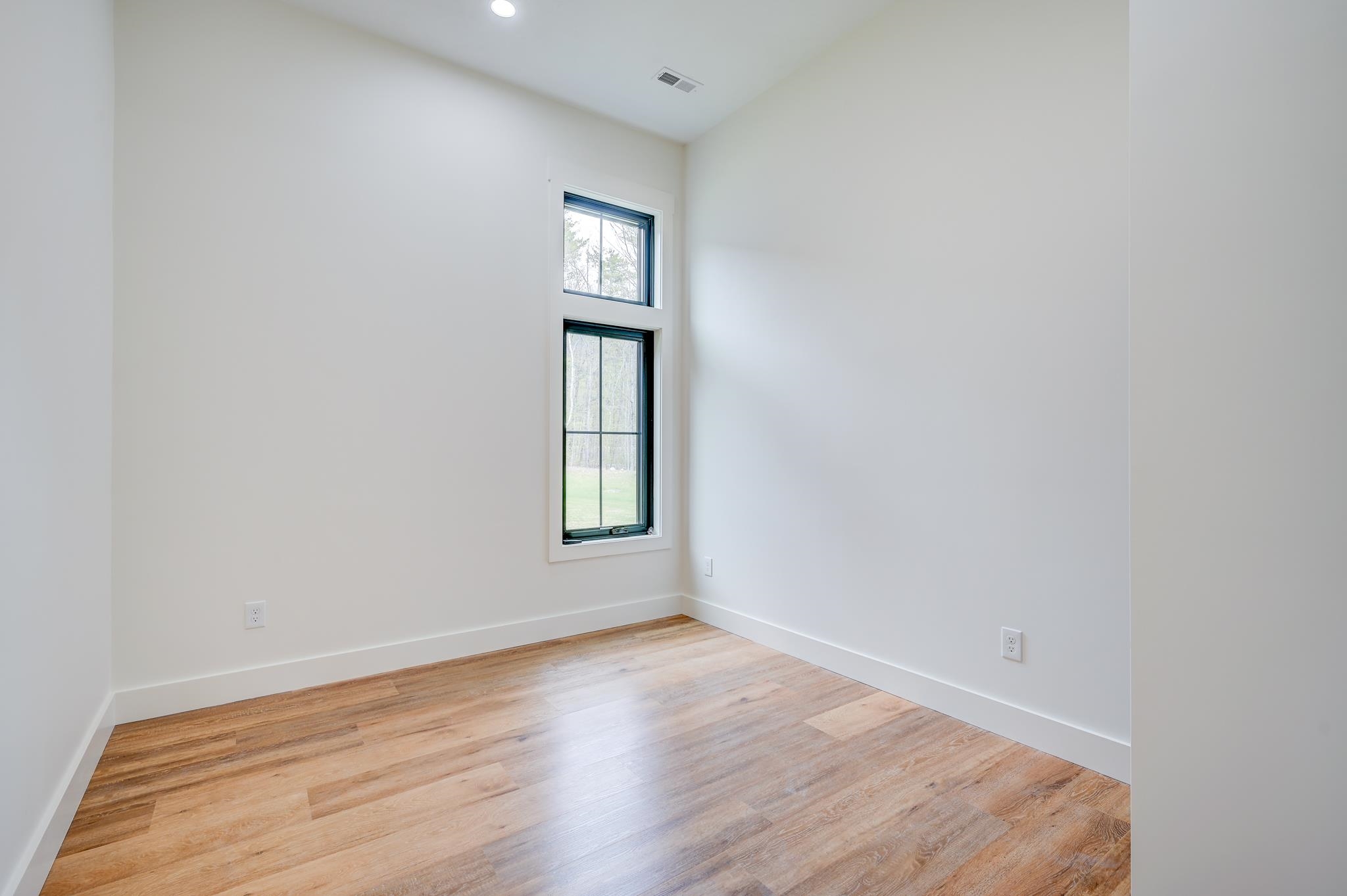 Empty room with light wood floors and tall stacked windows overlooking trees and lawn.