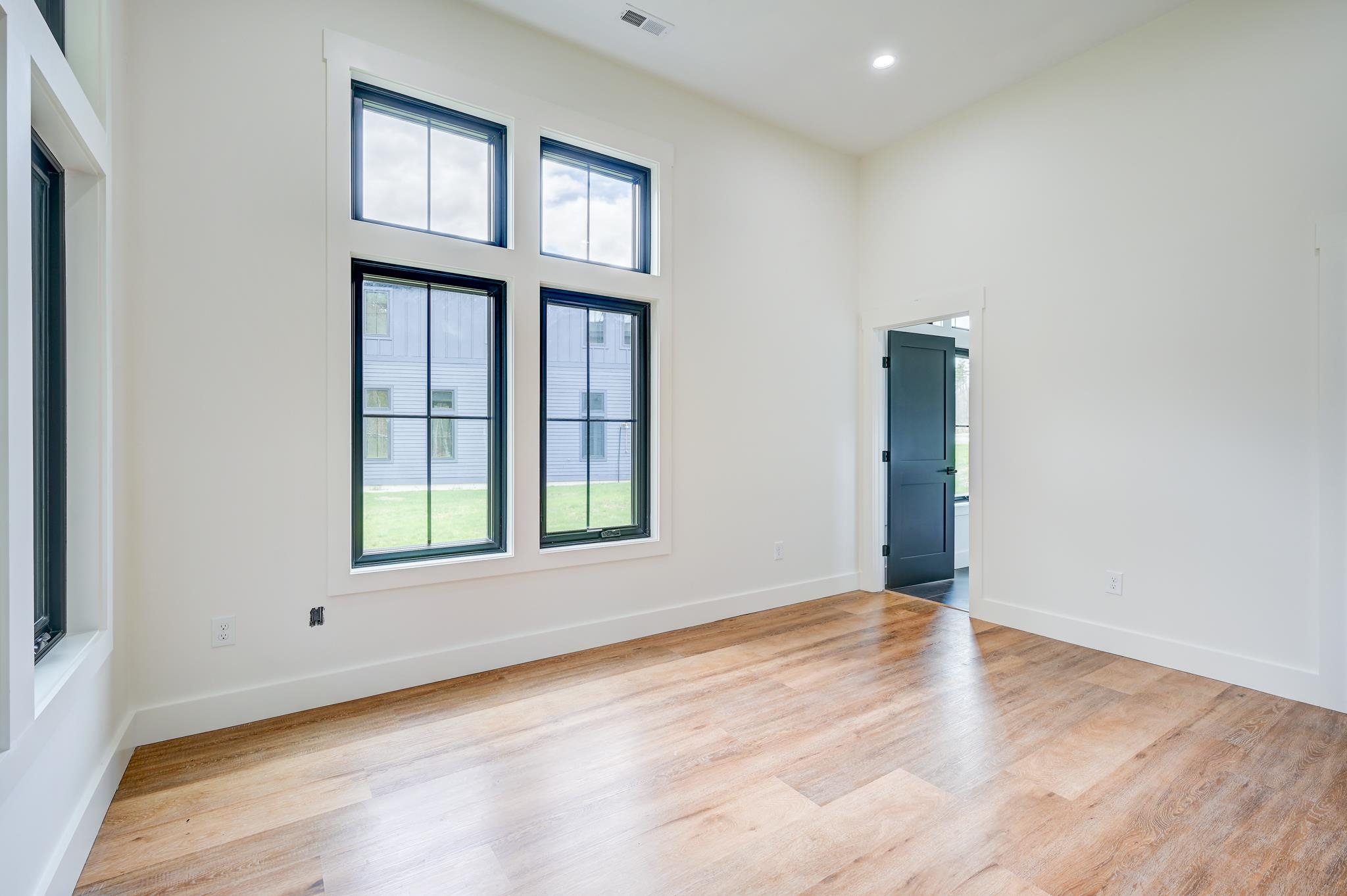 Empty room with tall black-trimmed windows, light wood floors, and a dark blue door.