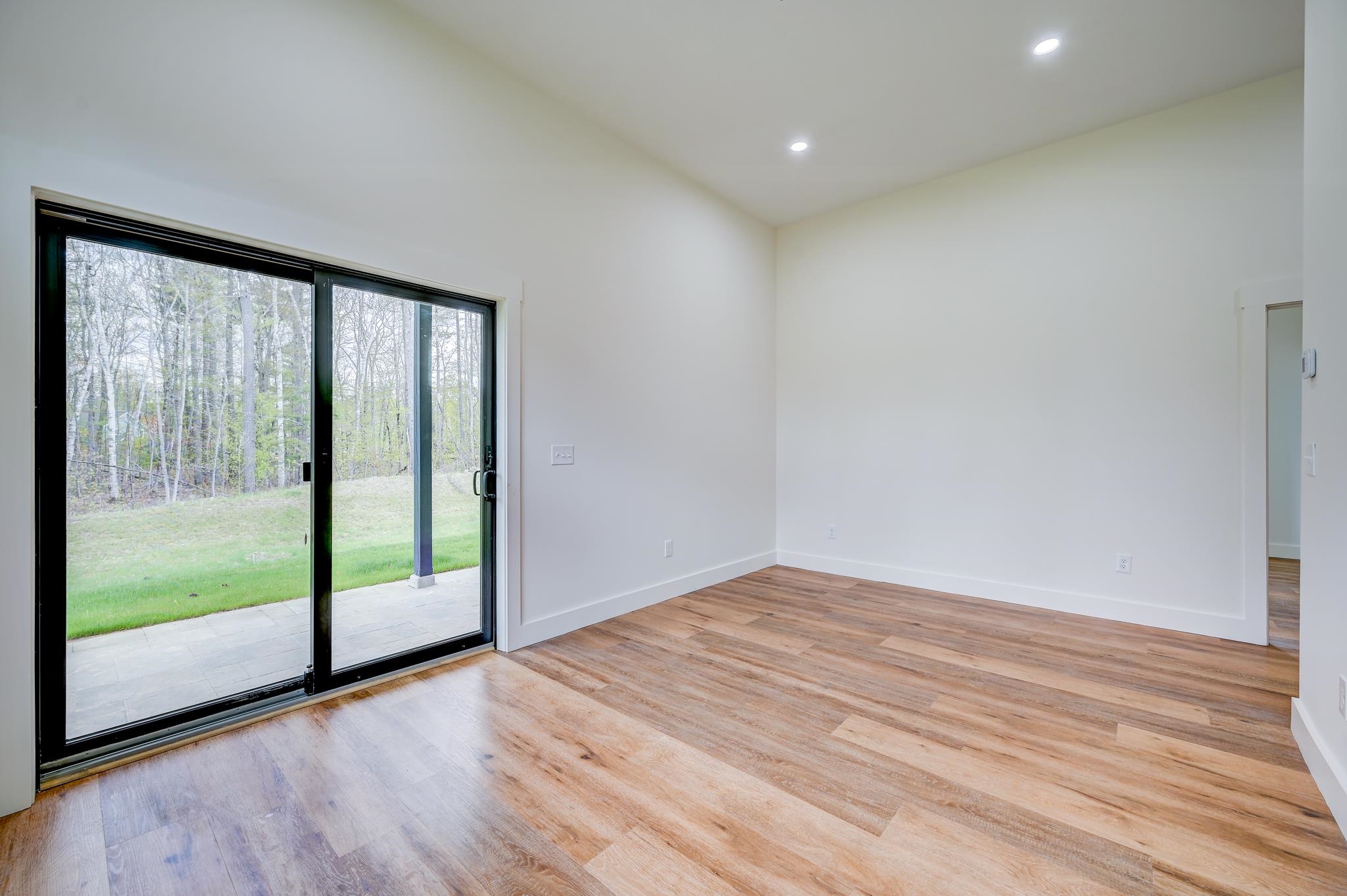 Empty room with wood-look floors and a sliding glass door opening to a patio and wooded yard.