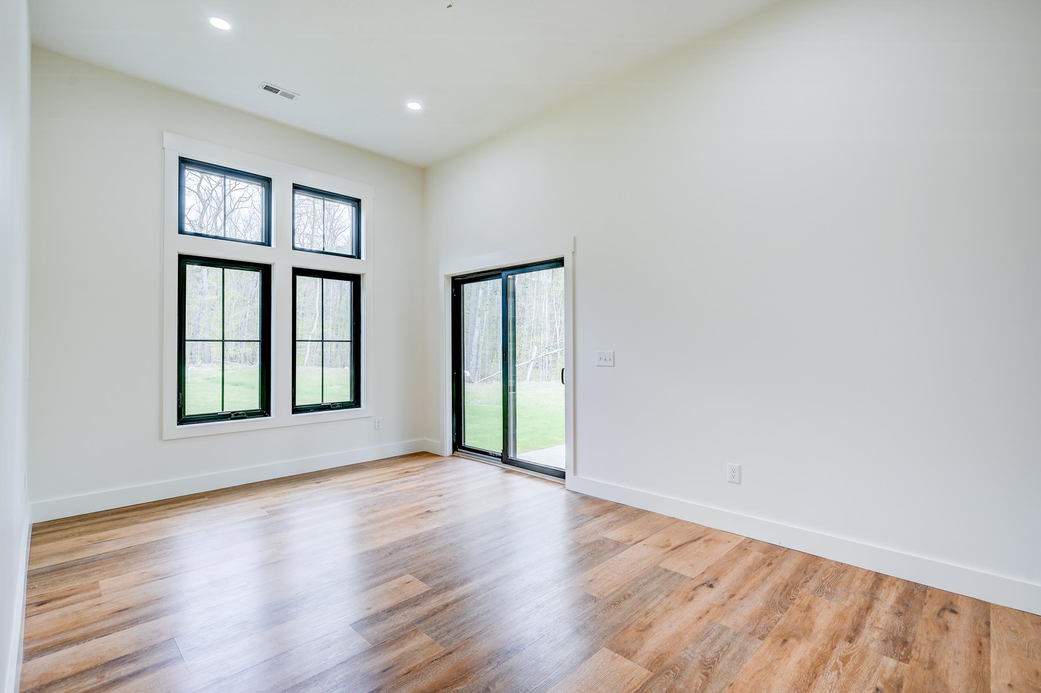 Empty room with wood-look floors, tall windows, and a sliding glass door to the yard.