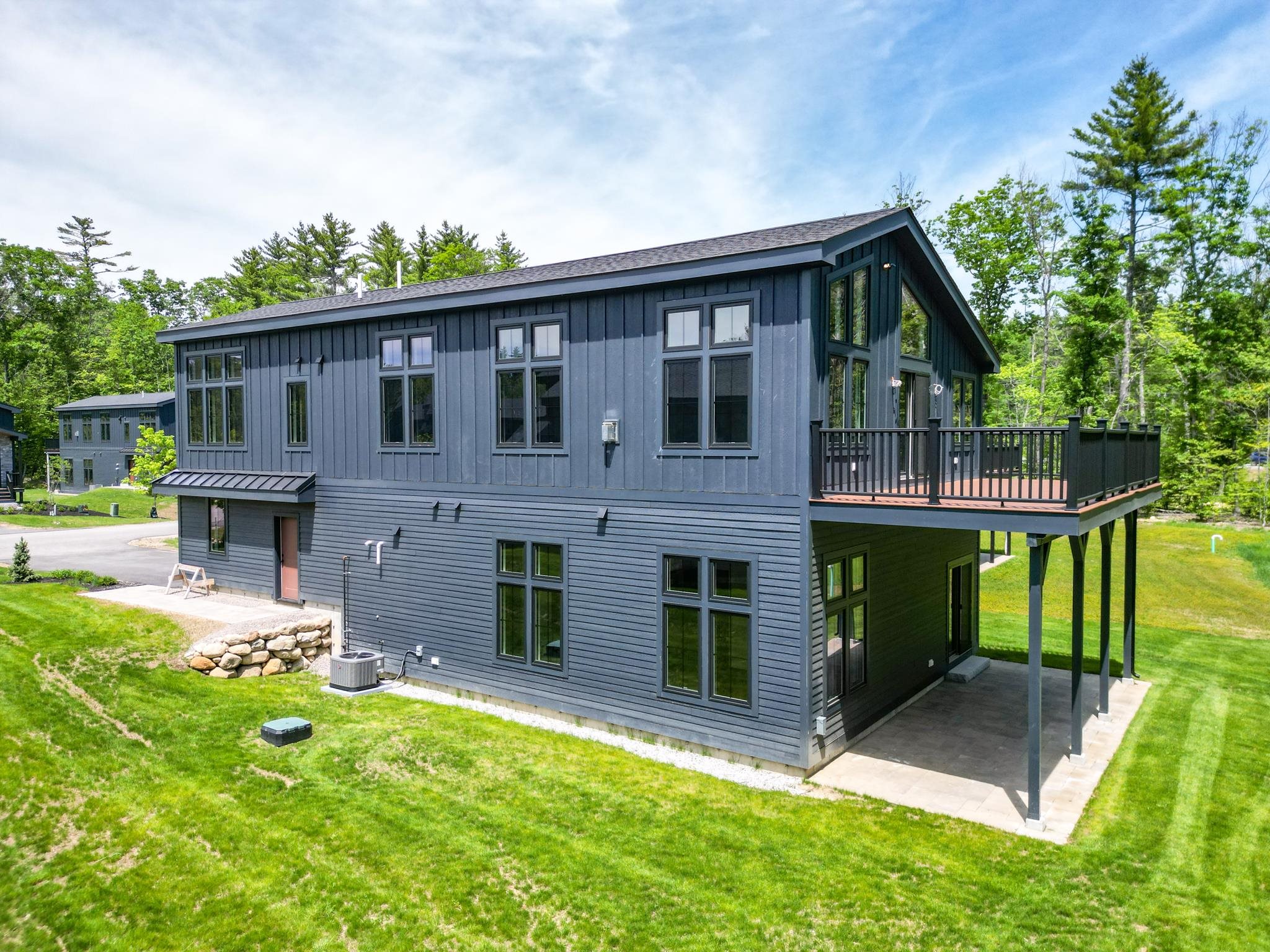 Modern dark blue-gray home with large windows and a raised deck overlooking a green lawn.