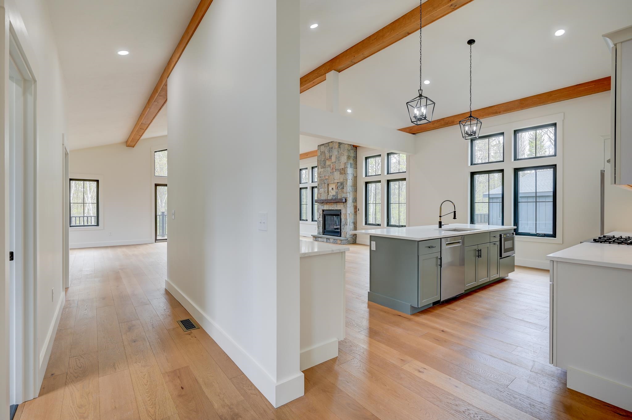 Open kitchen with gray island, vaulted wood-beamed ceiling, and stone fireplace.