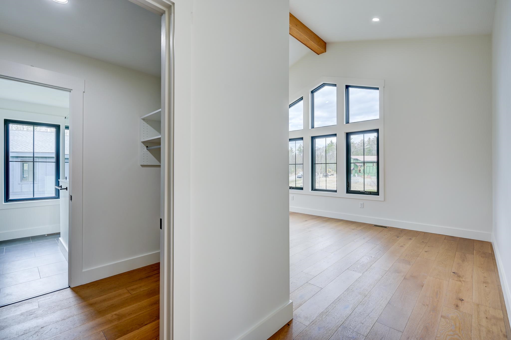 Bright empty room with oak floors, tall windows, and an exposed ceiling beam.