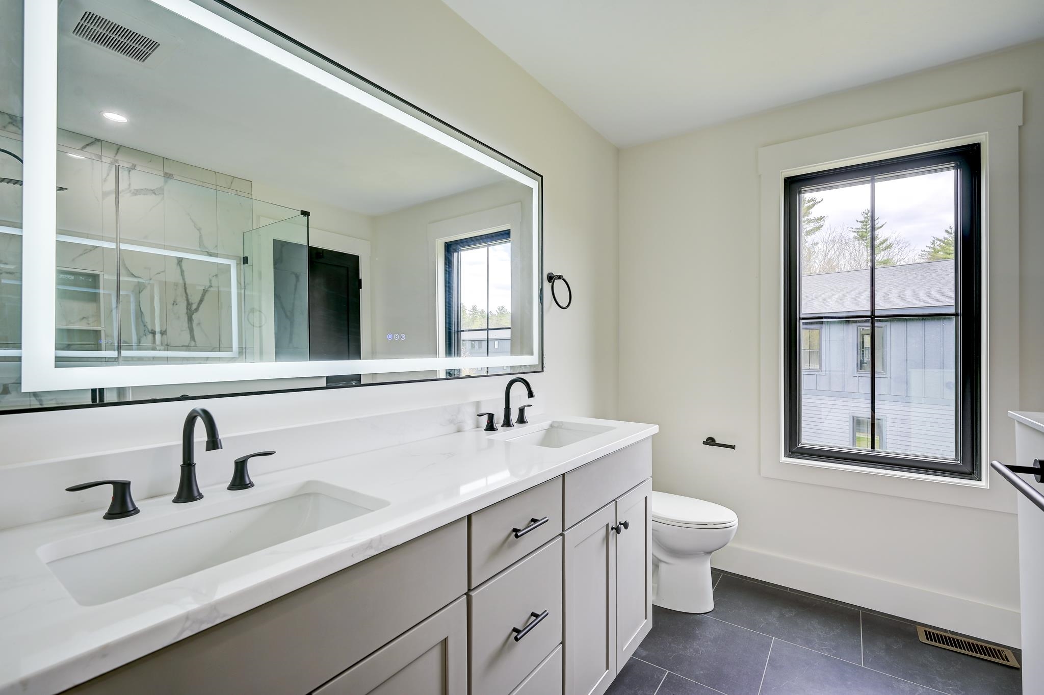 Modern bathroom with a double vanity, black fixtures, marble-look shower tile, and a large window.