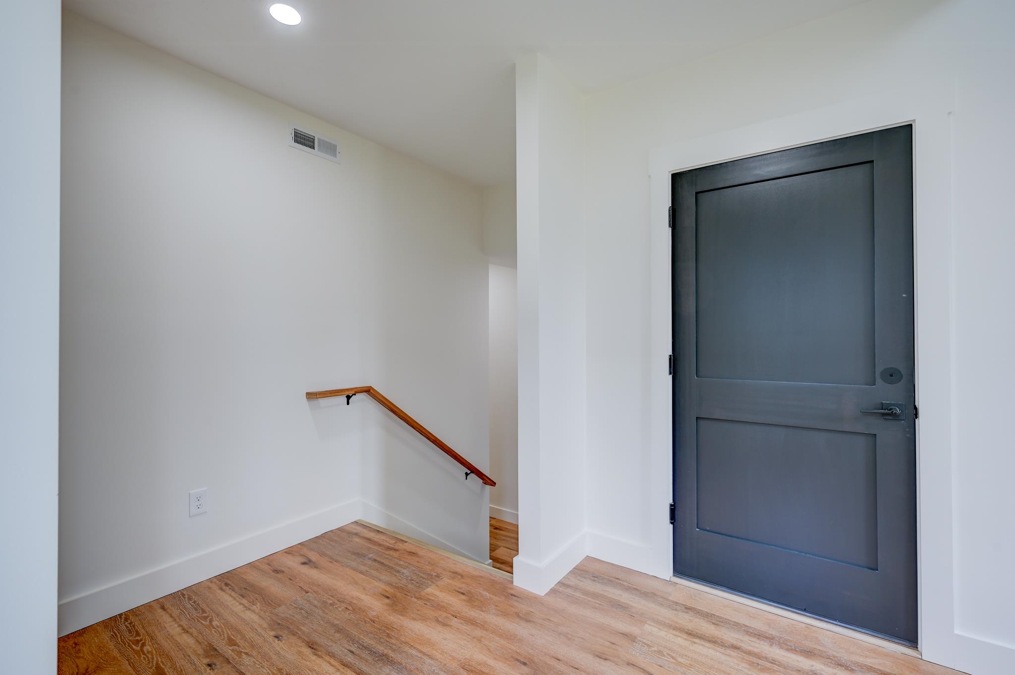 Entryway with a dark paneled front door, wood flooring, and a handrail beside the stairwell.