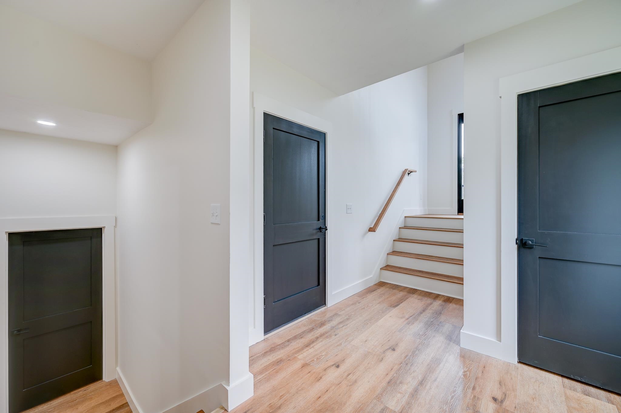 Entry foyer with dark doors, light wood-look flooring, and stairs with a wood handrail.