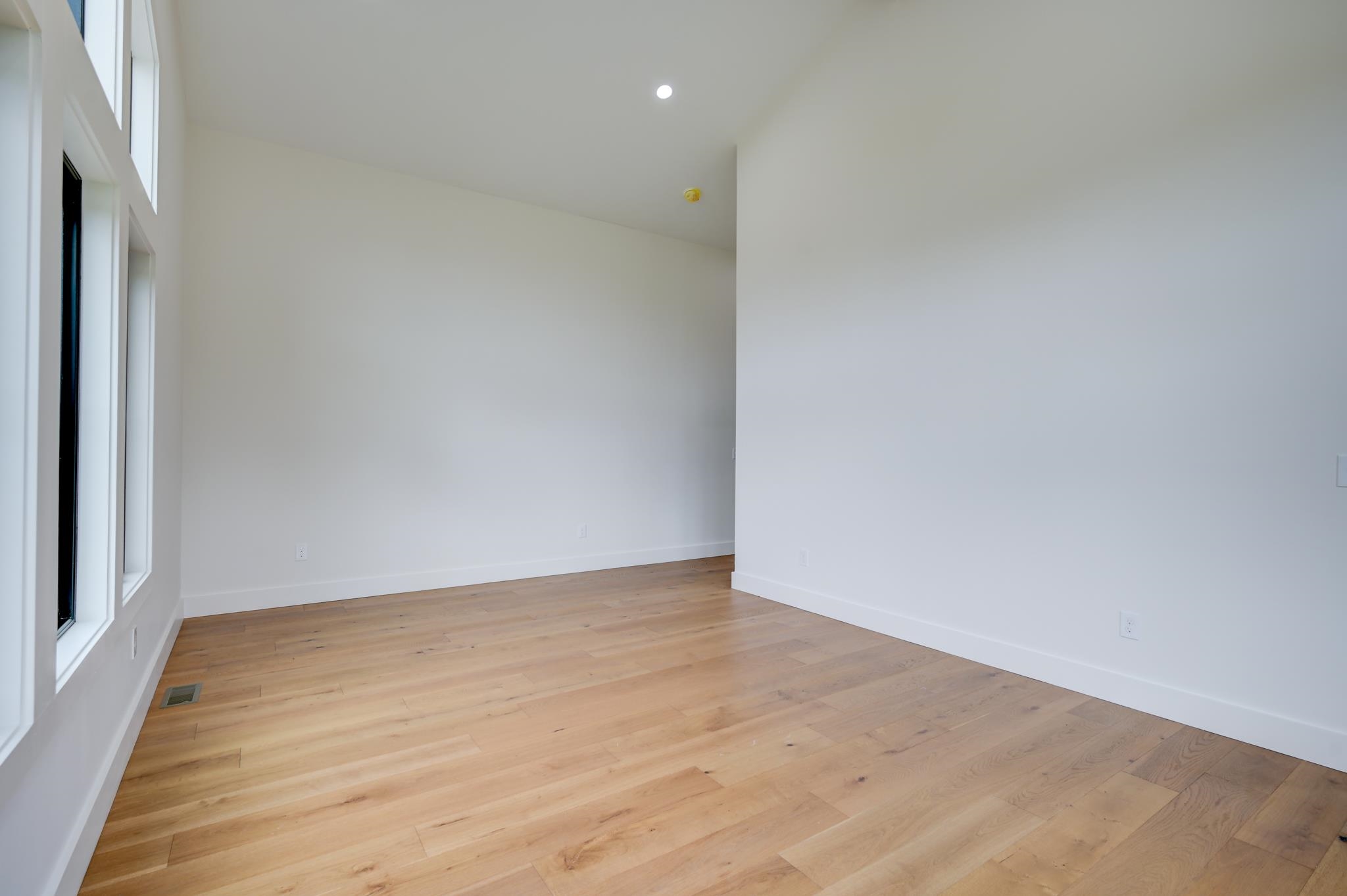Empty room with light wood floors and tall windows.