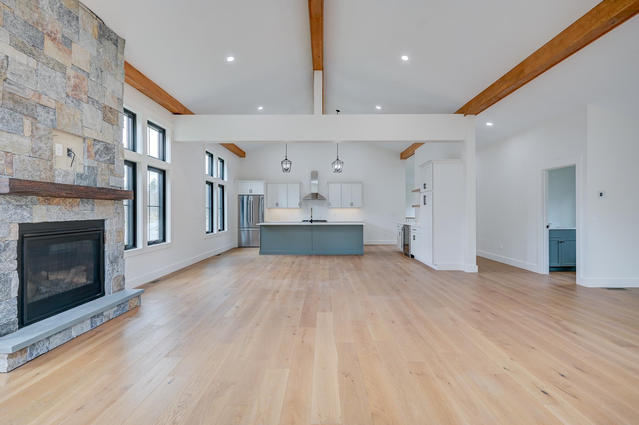 Open-plan kitchen and living room with a stone fireplace, vaulted wood-beam ceiling, and blue-gray island.
