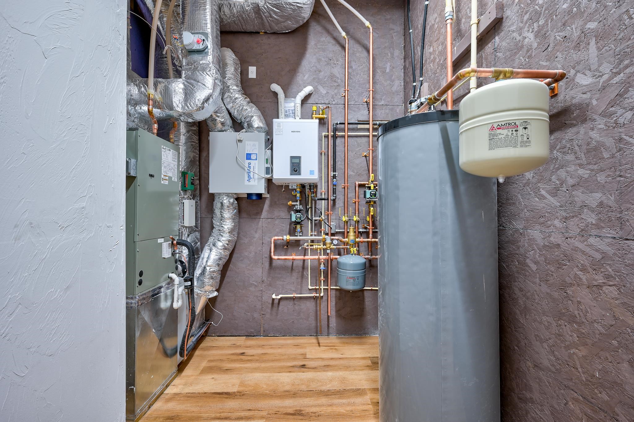 Mechanical room with a large water tank, heating equipment, and exposed copper pipes.