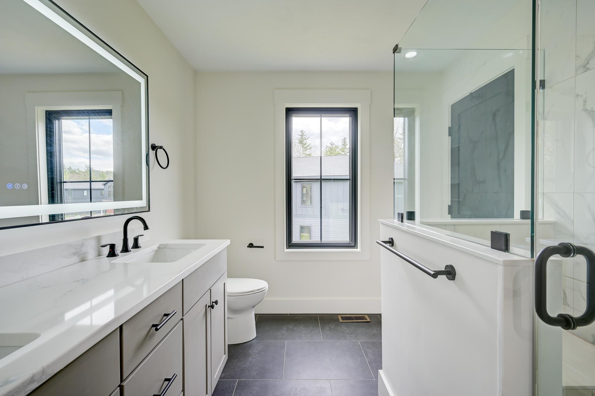 Modern bathroom with a long white vanity, black fixtures, and a glass shower beside a large window.