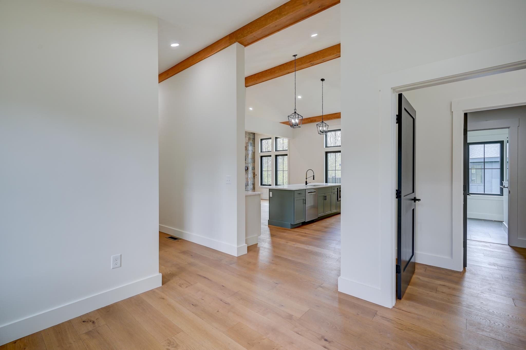 Open kitchen with a gray-green island, exposed wood beams, tall windows, and light hardwood floors.