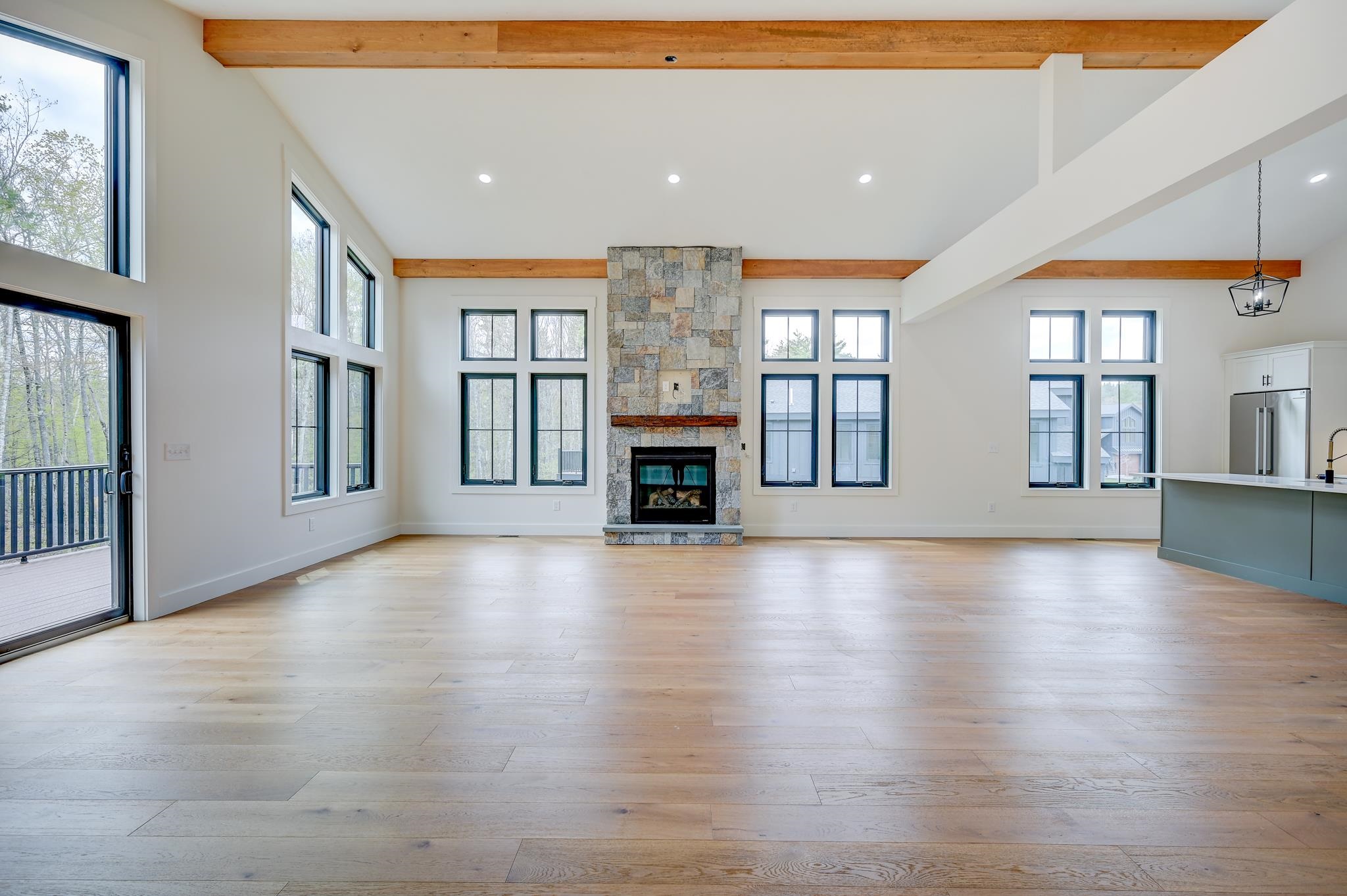 Vacant living room with a tall stone fireplace, exposed wood beams, and large windows.