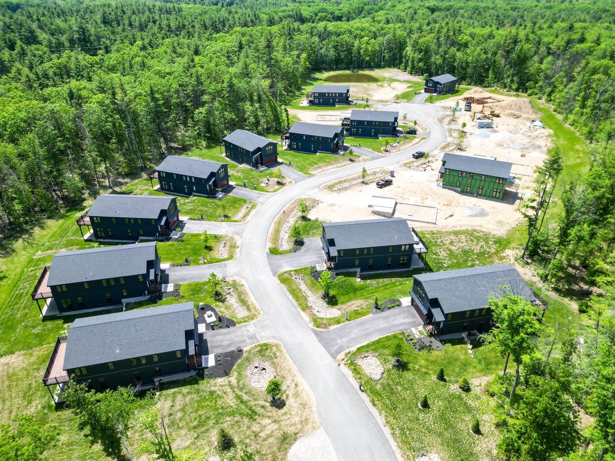 Aerial view of modern homes in a wooded development, with cleared construction lots beside a curved road.