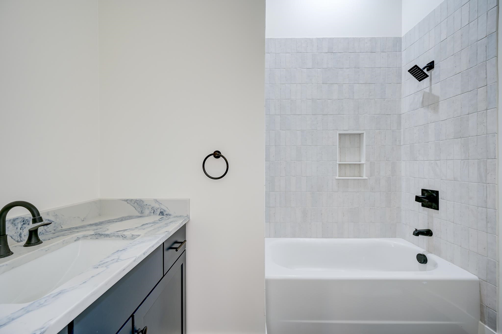 Modern bathroom with a white tub, gray tile, black fixtures, and marble-pattern vanity counter.
