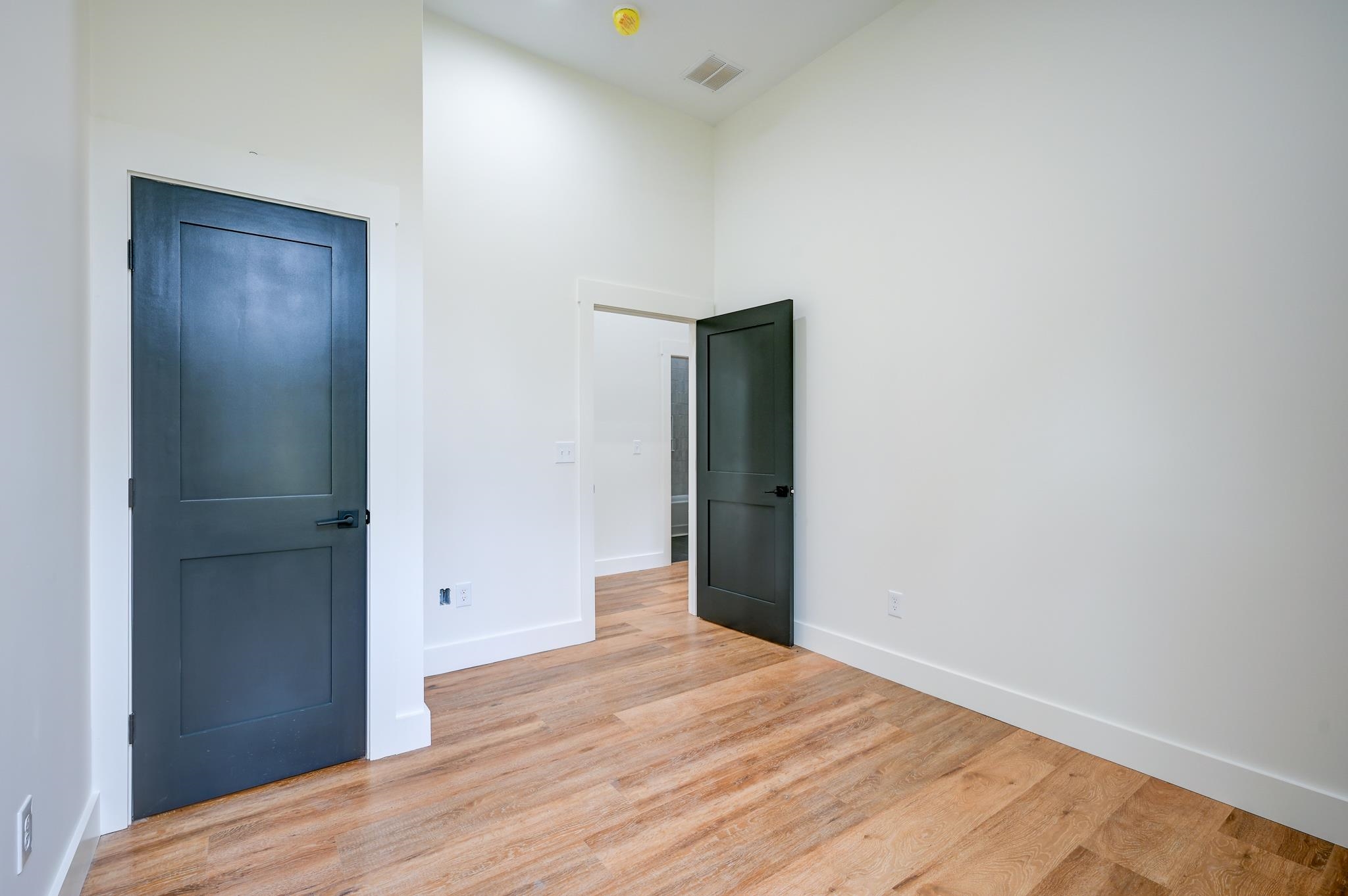 Empty room with warm wood floors, white walls, and two dark paneled doors.