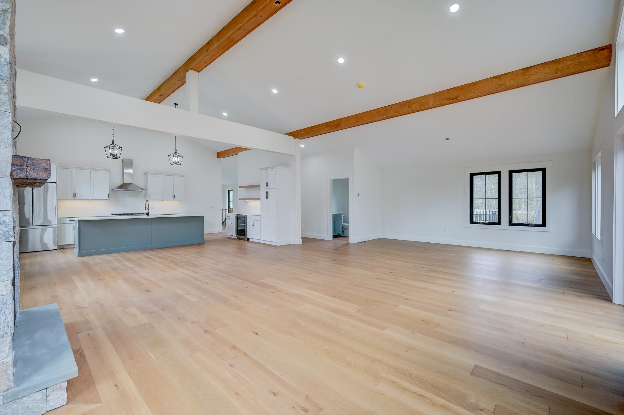 Open-plan kitchen and living room with timber beams, blue-gray island, pale wood floors, and stone fireplace.
