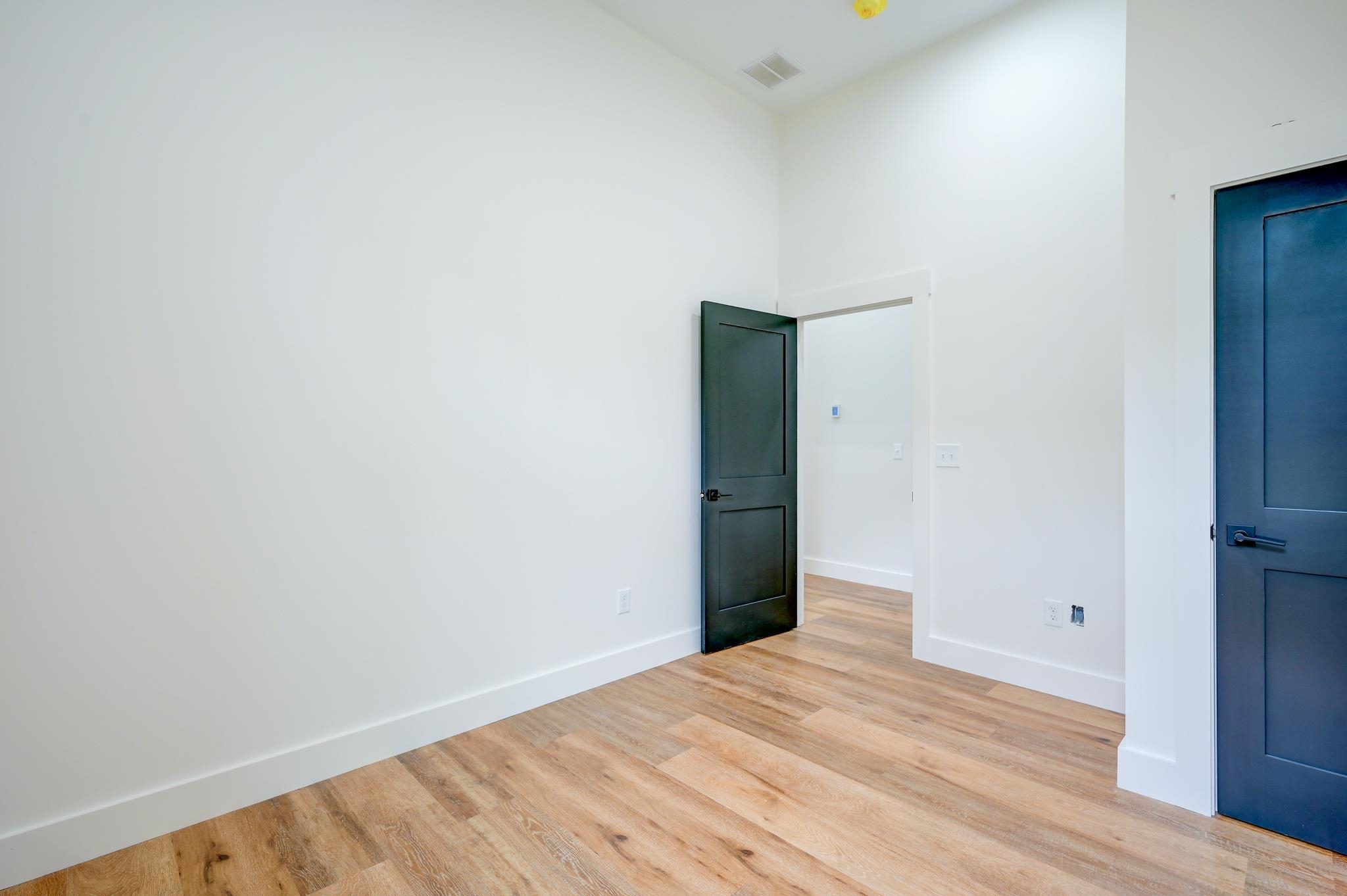 Empty room with light wood floors and dark blue doors, one open to a hallway.