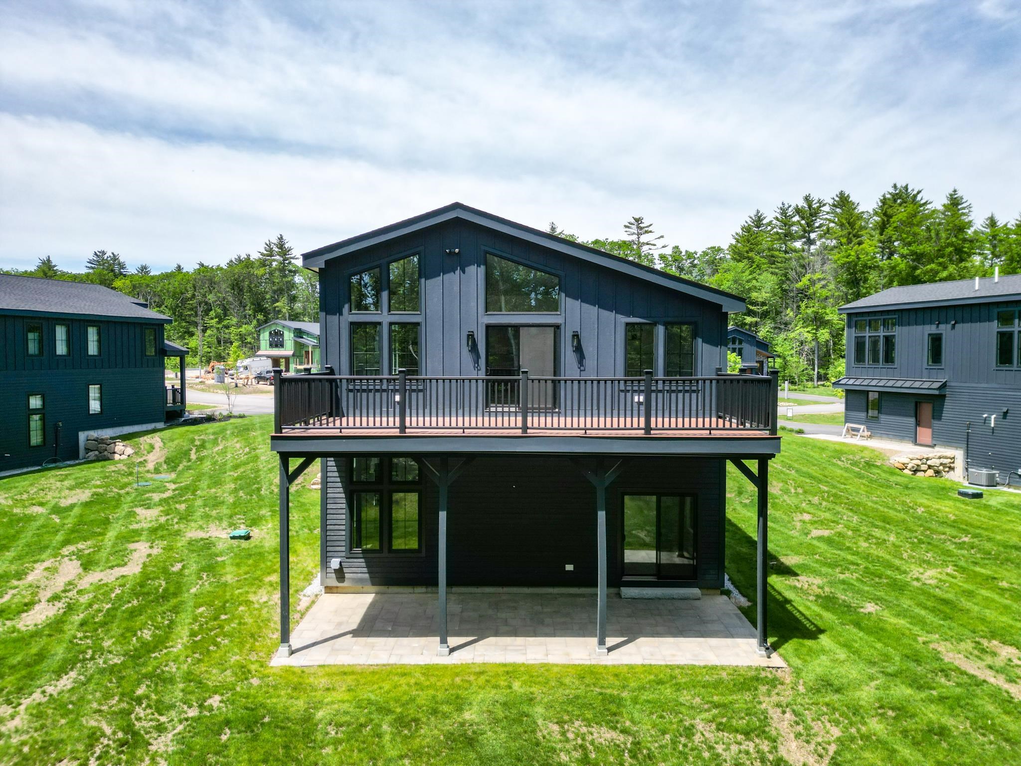 Modern dark-sided home with an elevated deck and covered patio overlooking a green lawn.