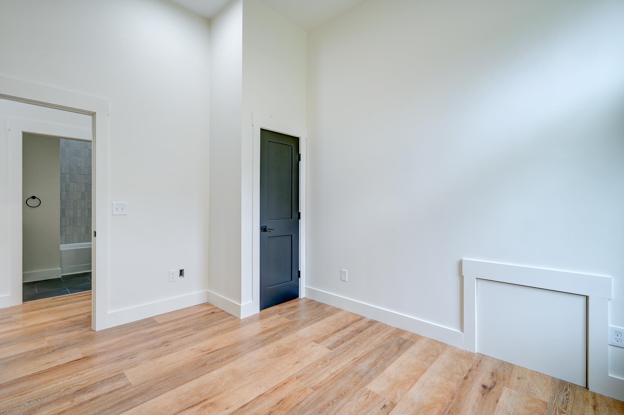 Unfurnished room with light wood floors, a dark paneled door, and an adjoining tiled bathroom.