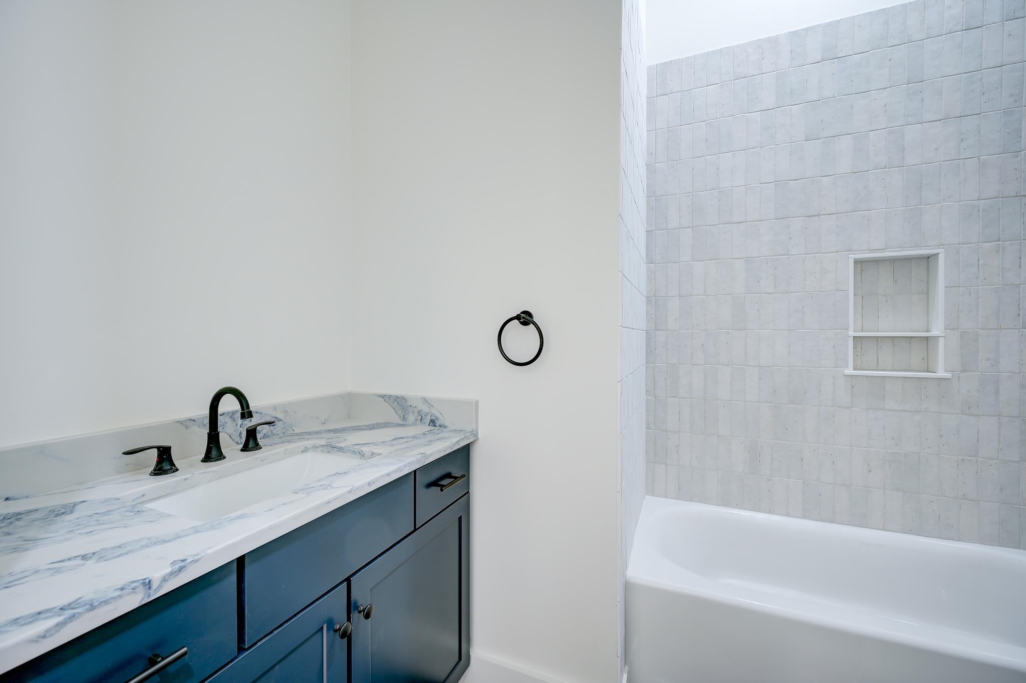 Bathroom with a navy vanity, veined marble countertop, and white bathtub with tiled surround.