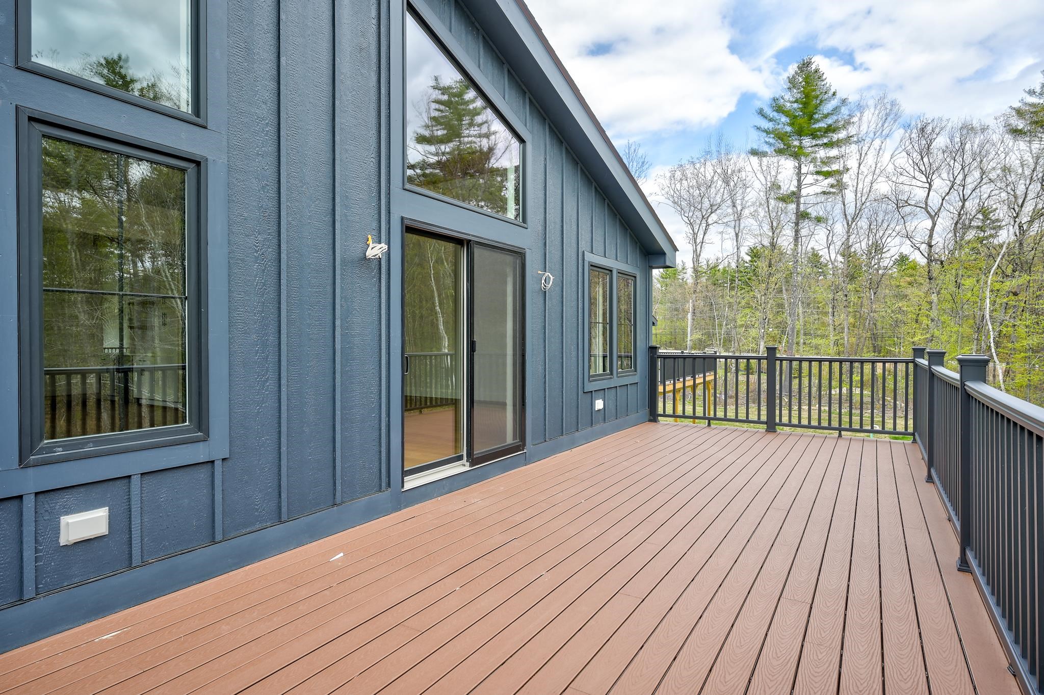 Spacious deck beside a blue-sided home, with black railings and a wooded view.