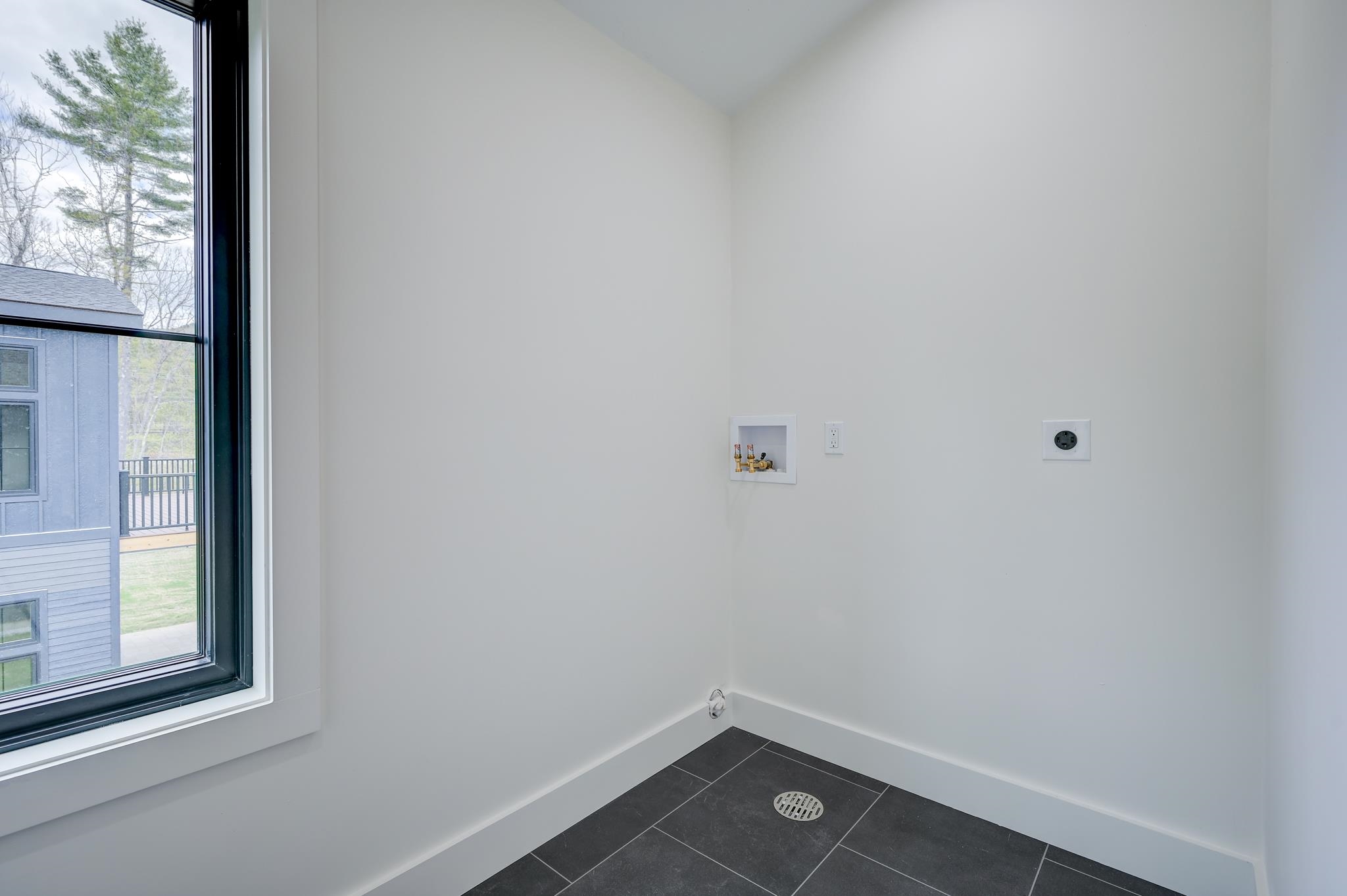 Empty laundry room with washer hookups, dark tile floor, and a large window.