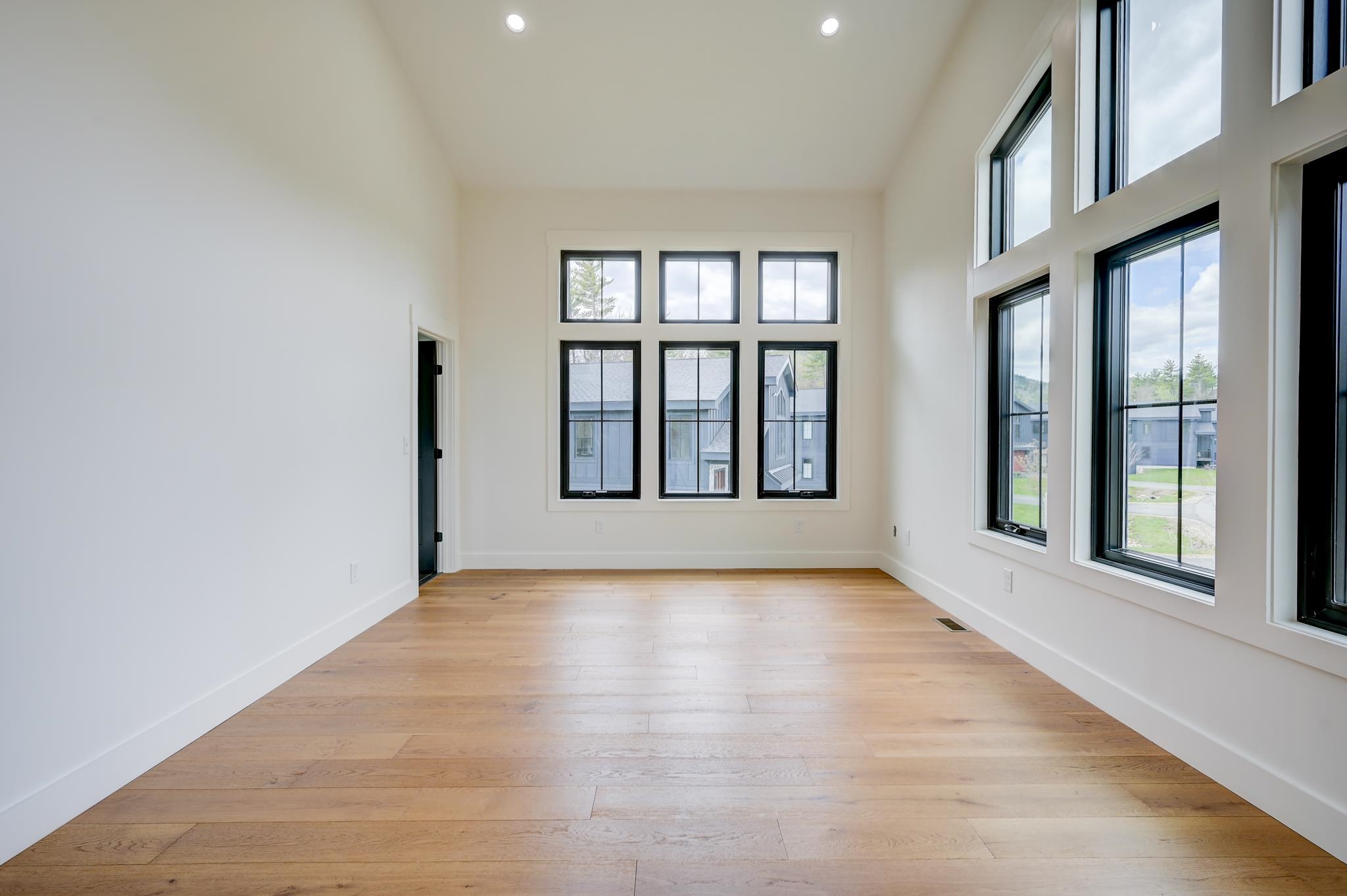 Empty room with light wood floors and tall black-framed windows.