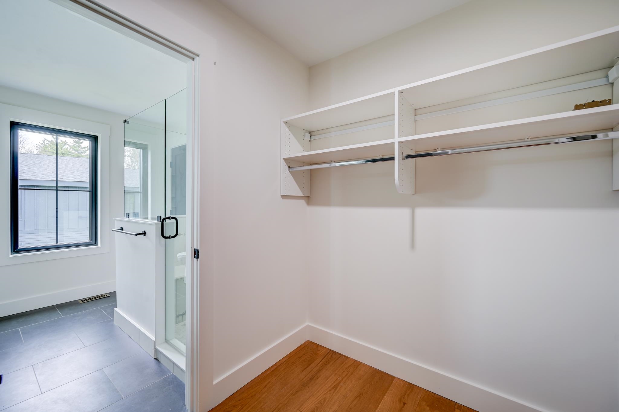 Walk-in closet with white shelving and hanging rods beside a glass-enclosed shower.