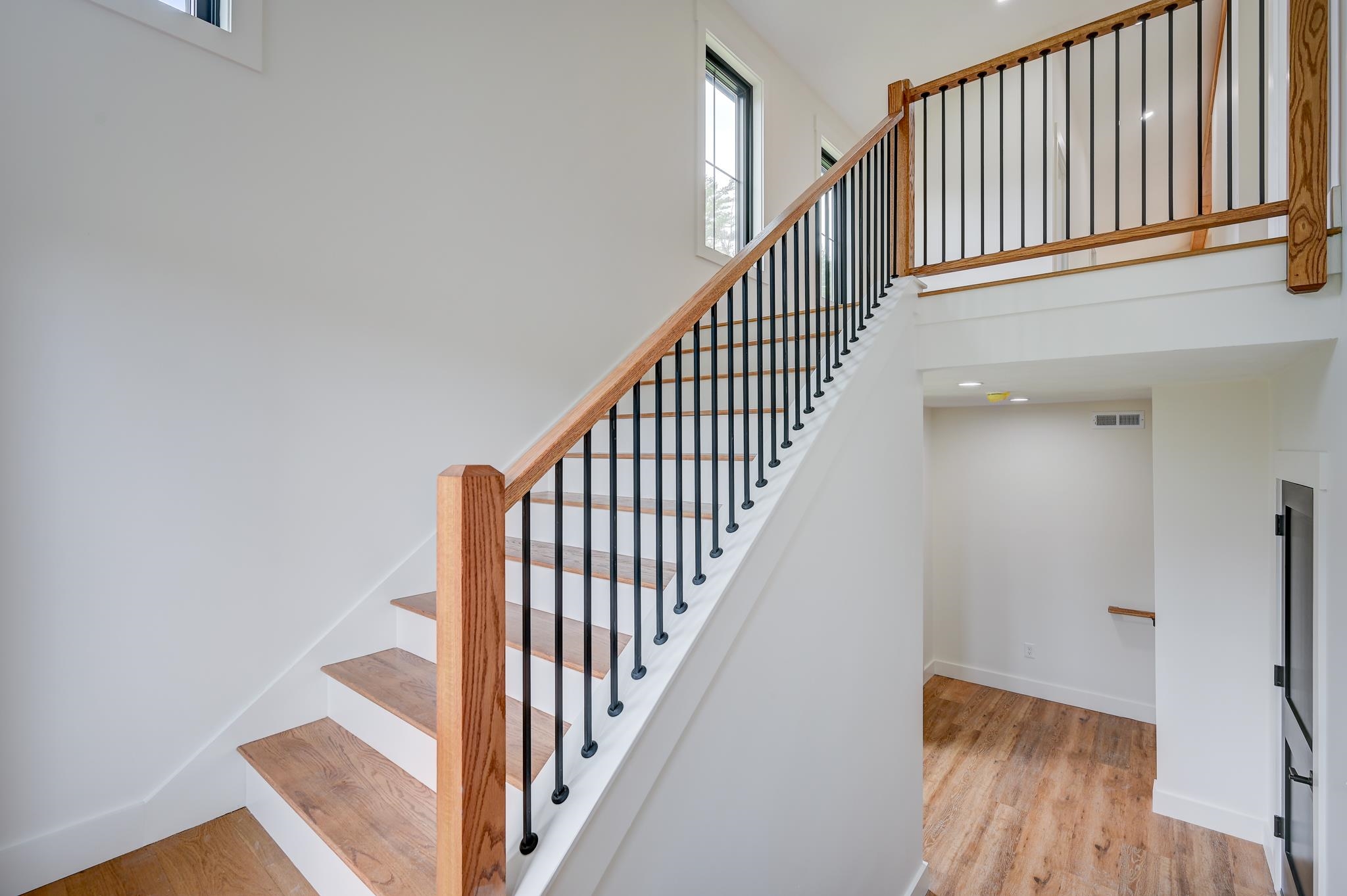 Interior staircase with wood treads, a natural wood handrail, and black metal balusters.