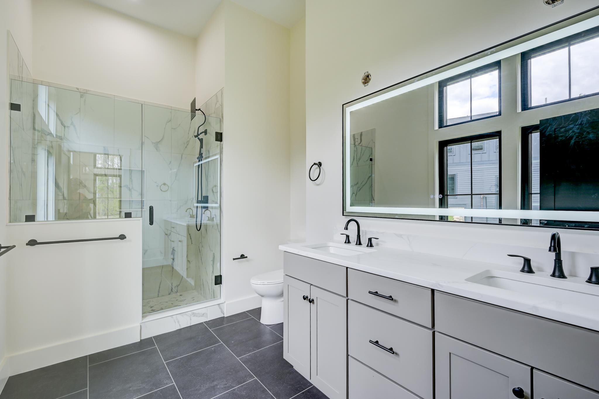 Modern bathroom with a marble-look glass shower and long white double vanity.