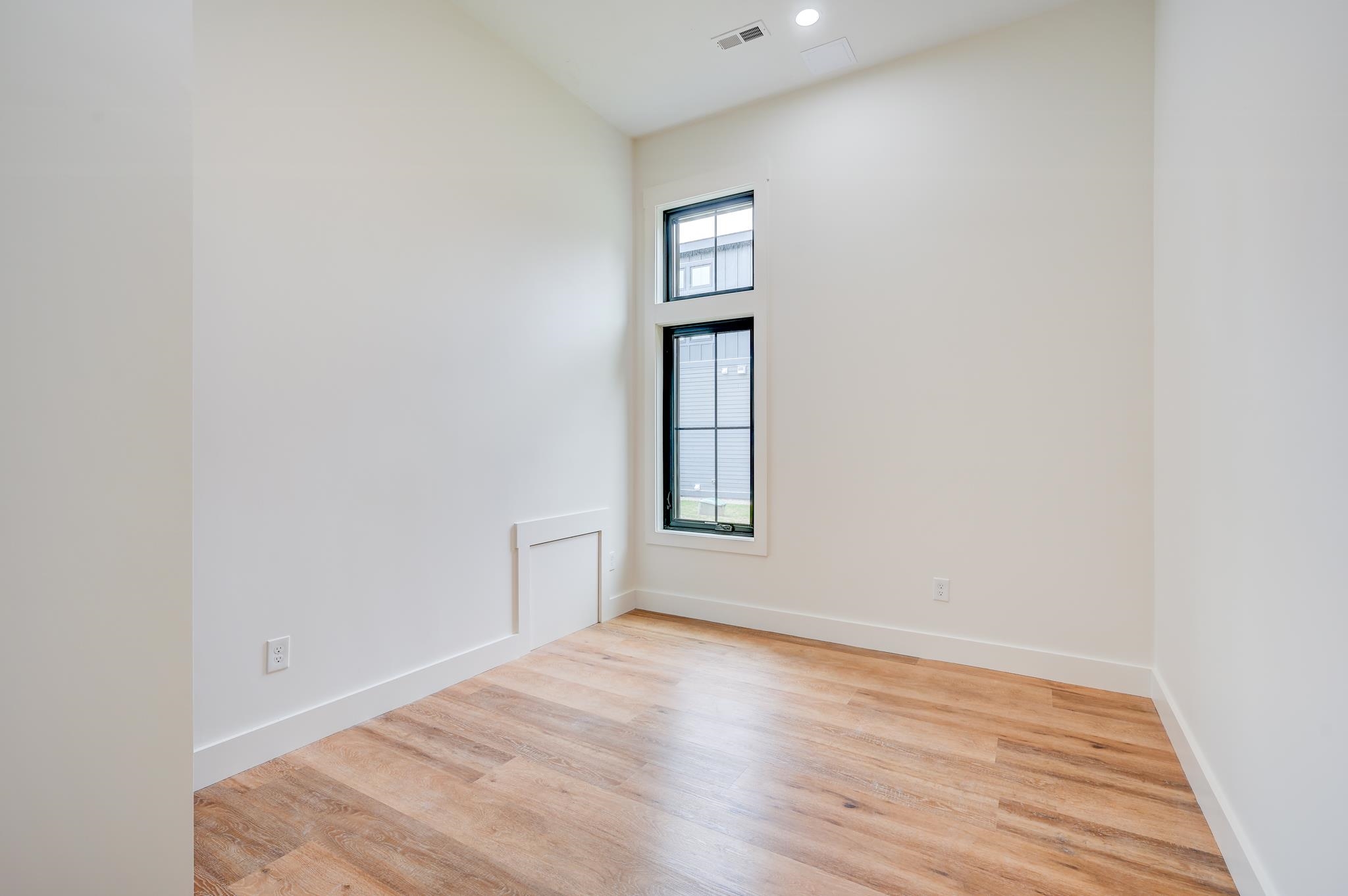 Empty room with light wood floors, a high ceiling, and two stacked windows.