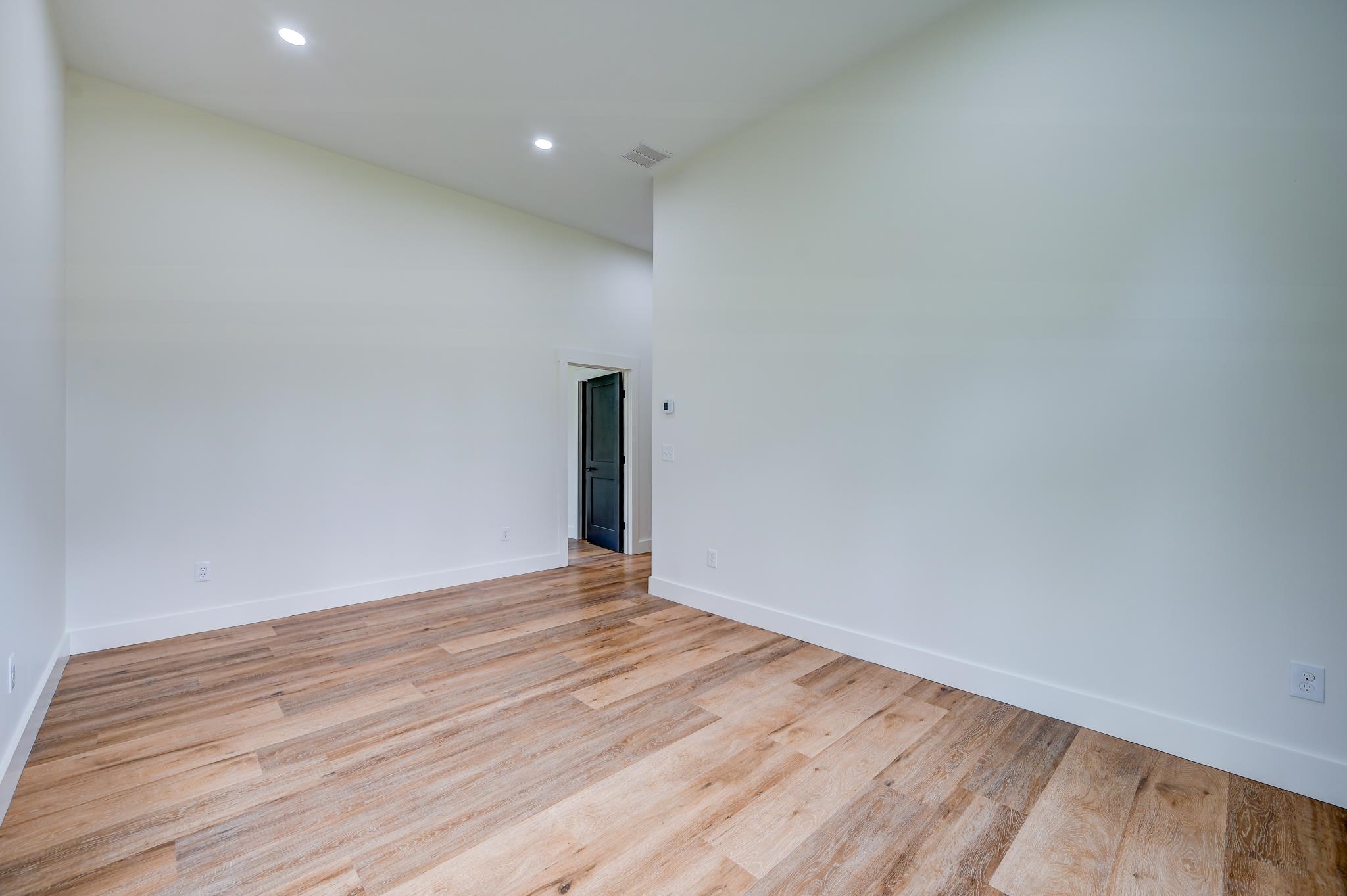 Empty room with white walls, wood-look plank flooring, and a dark doorway.
