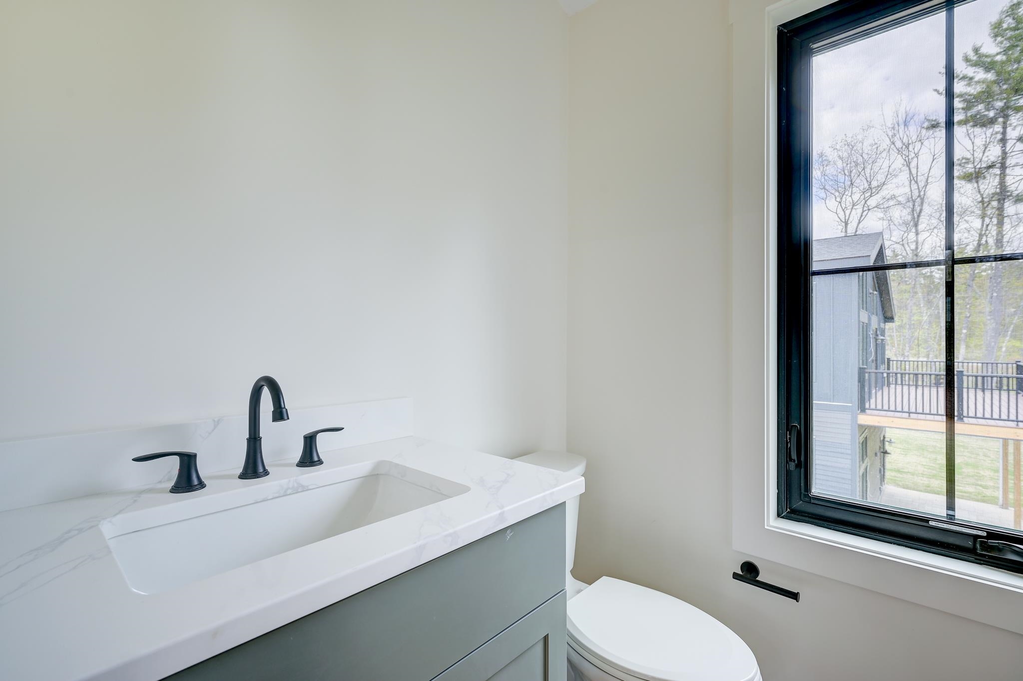 Modern bathroom vanity with a marble-look sink, black faucet, and large window beside the toilet.