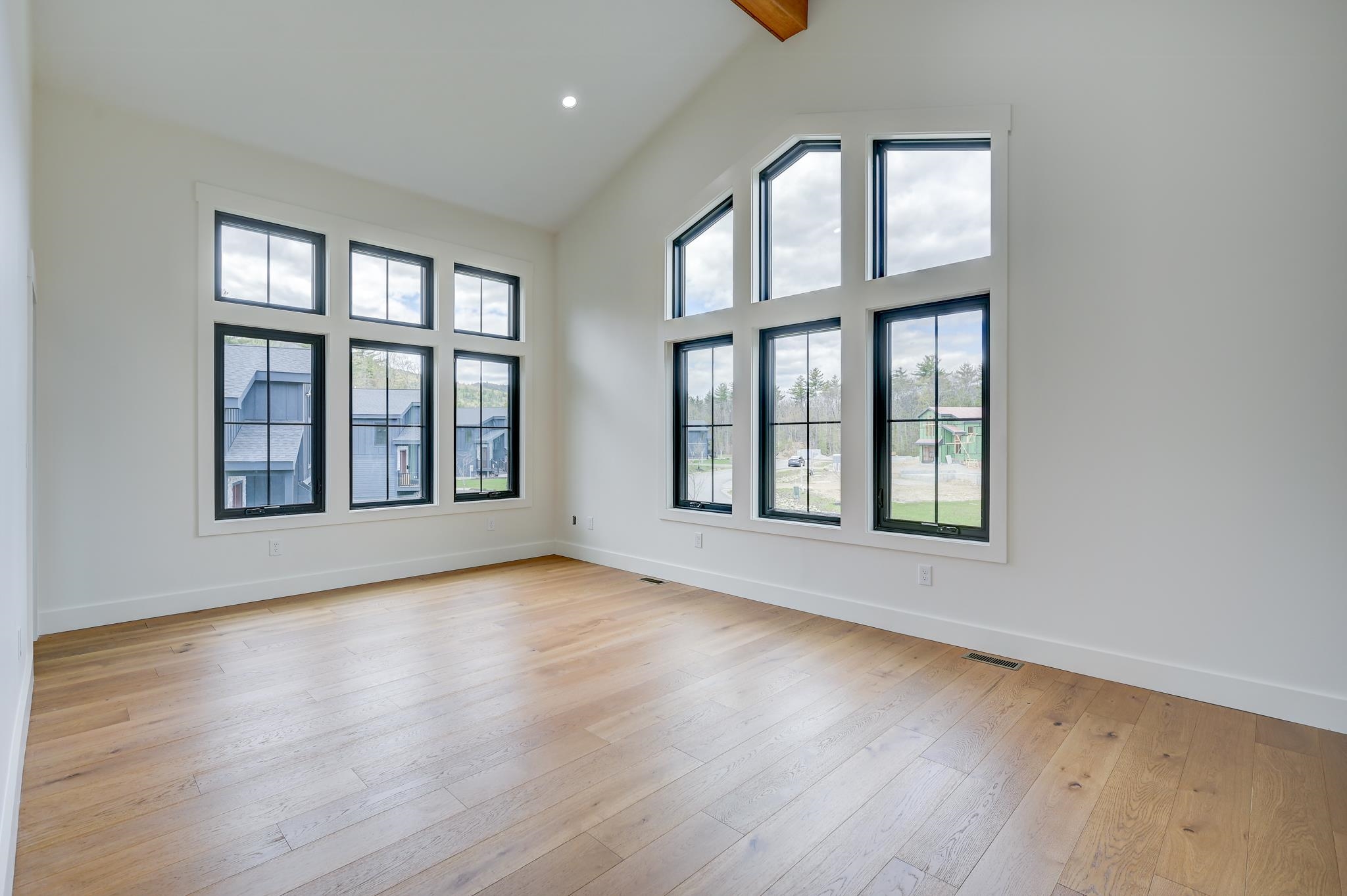 Empty room with a vaulted ceiling, pale wood floors, and large windows on two walls.