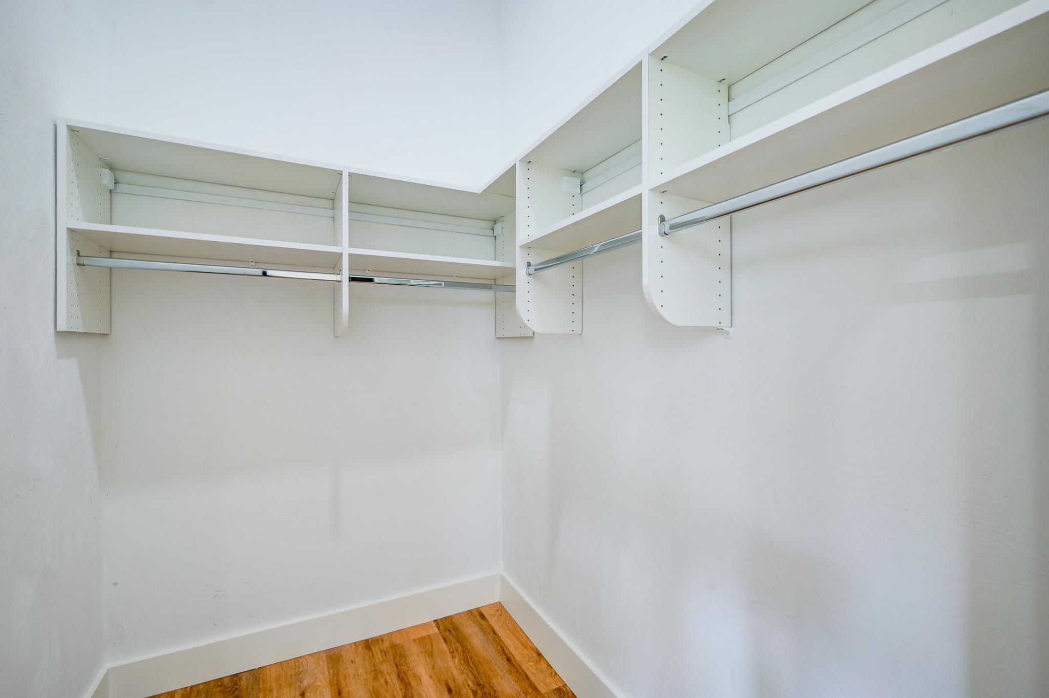 Walk-in closet with white shelving, hanging rods, and a wood floor.