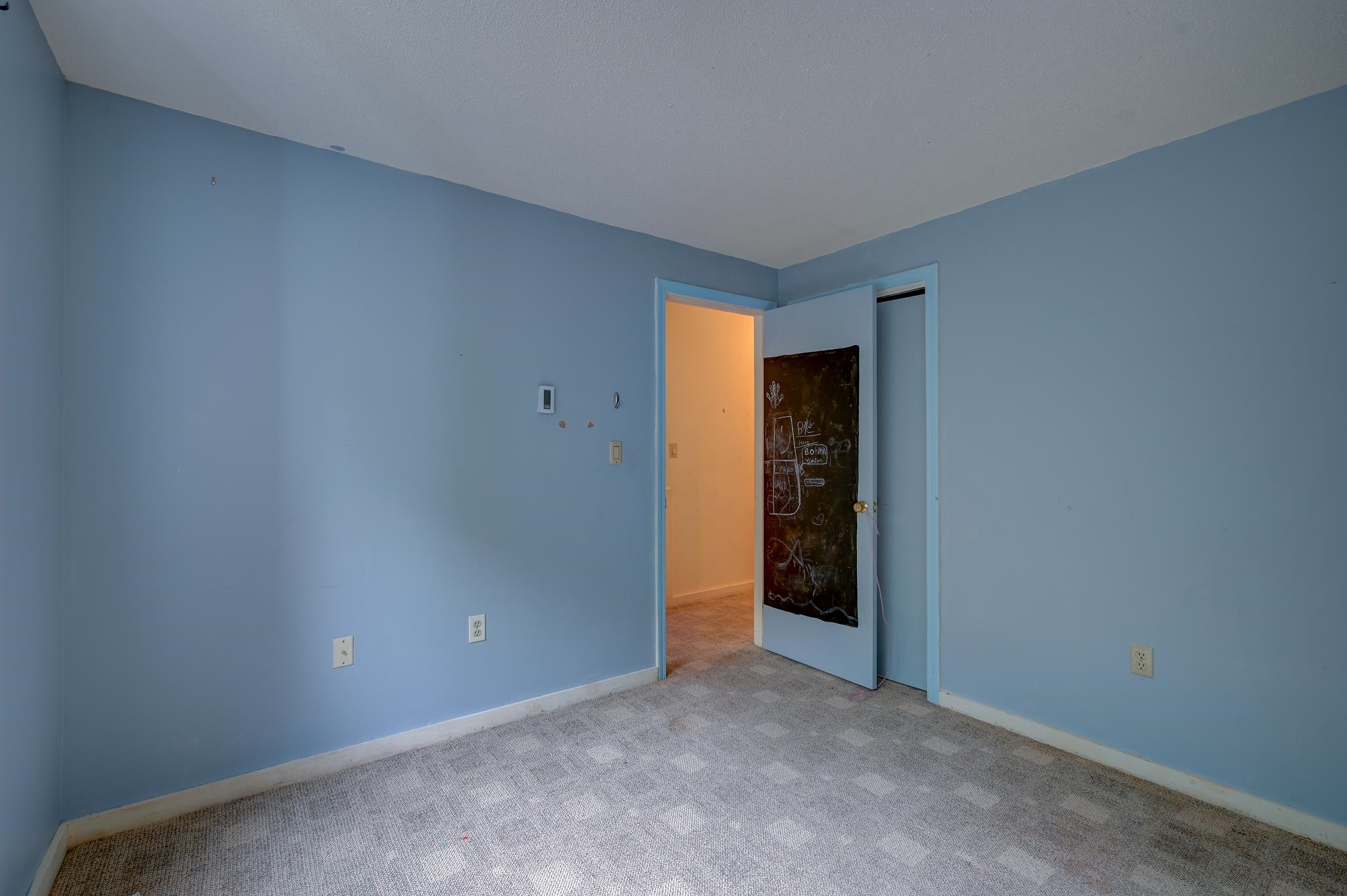 Empty blue-walled room with gray carpet and an open door bearing chalk drawings.