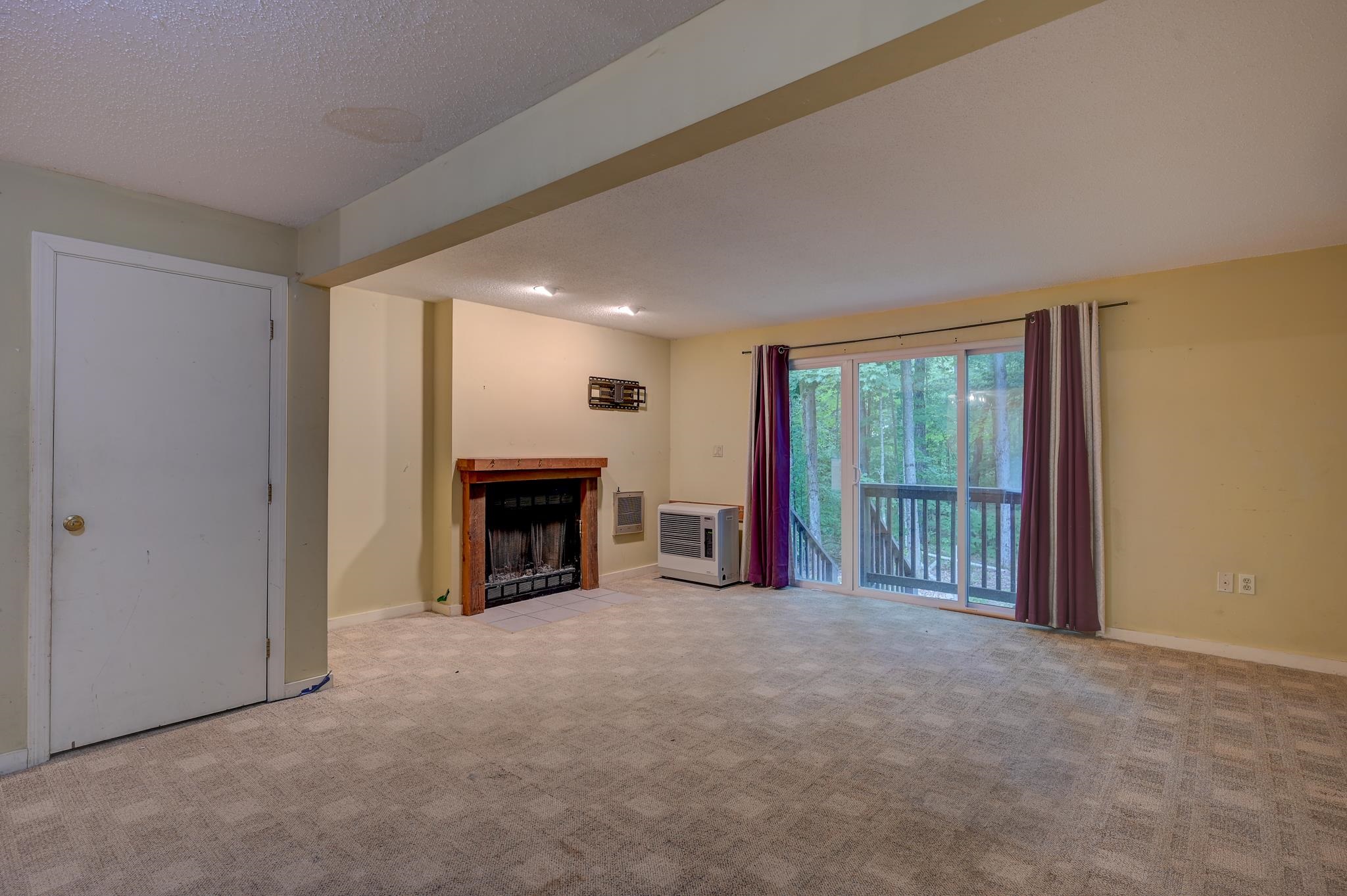Unfurnished living room with a wood-trimmed fireplace and sliding doors to a wooded balcony.
