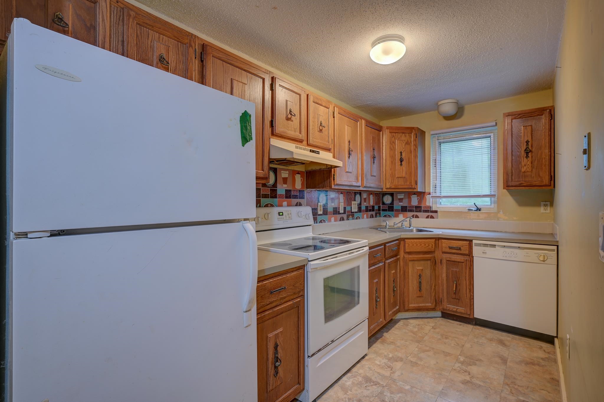 Kitchen with wood cabinets, patterned tile backsplash, and white appliances.