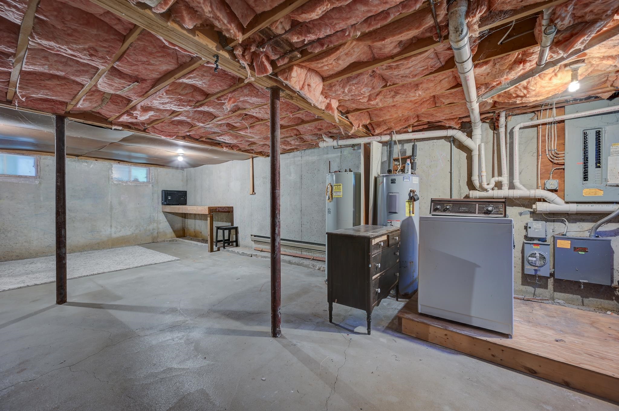 Unfinished basement with exposed ceiling insulation, concrete floor, washer and dryer, and utility equipment.