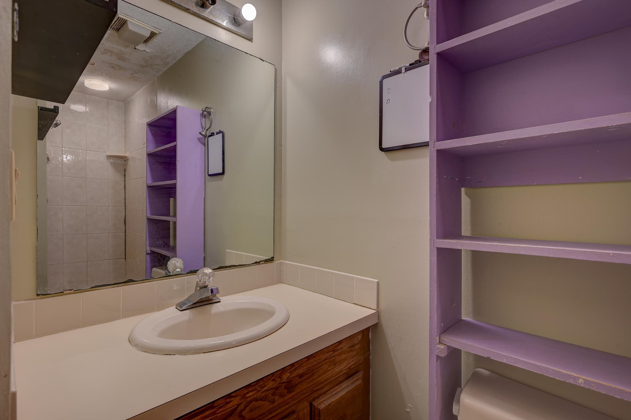 Bathroom vanity with an oval sink, large mirror, and purple open shelving.
