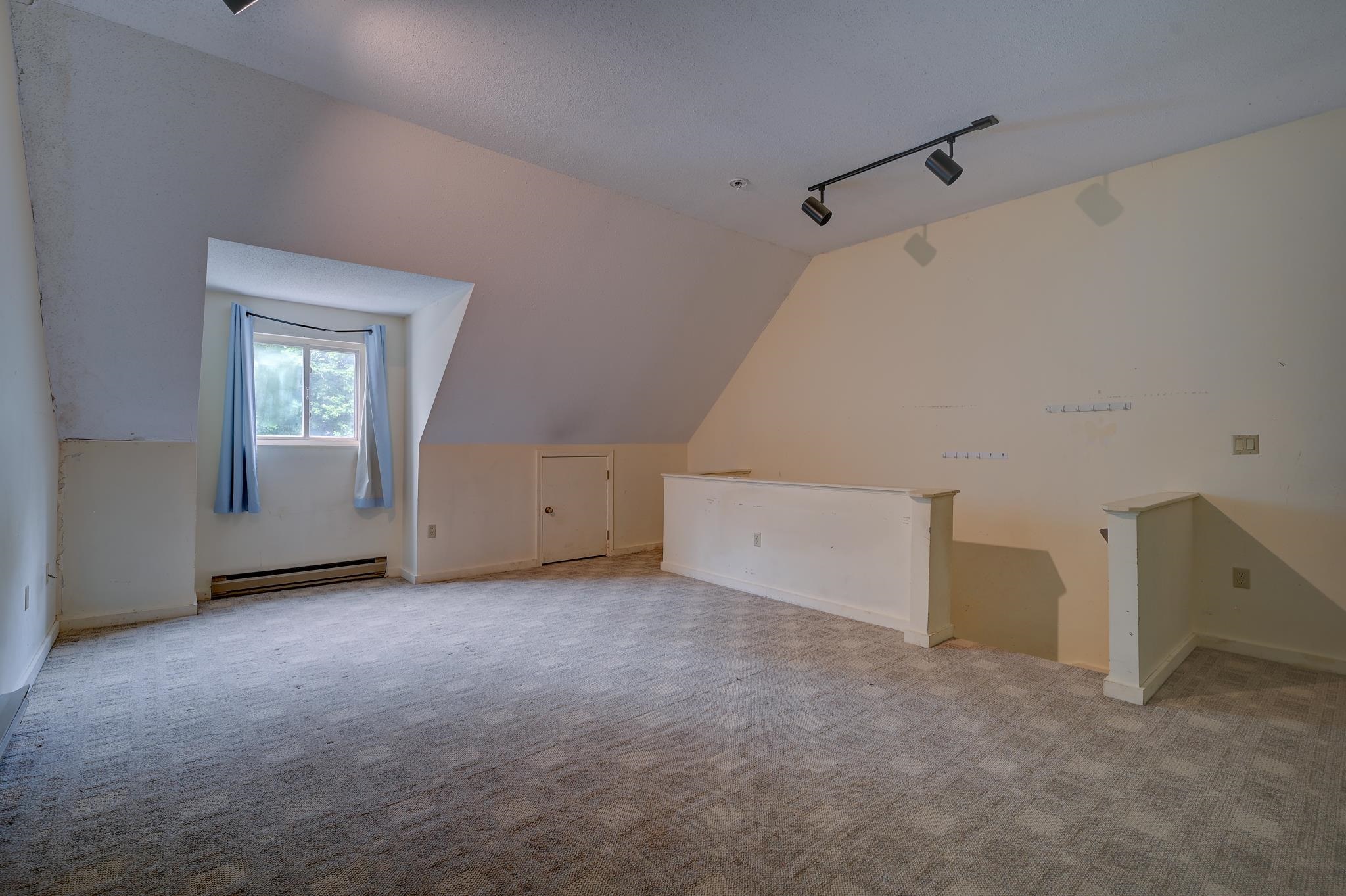 Vacant upper-level room with sloped ceilings, a curtained dormer window, and carpet.