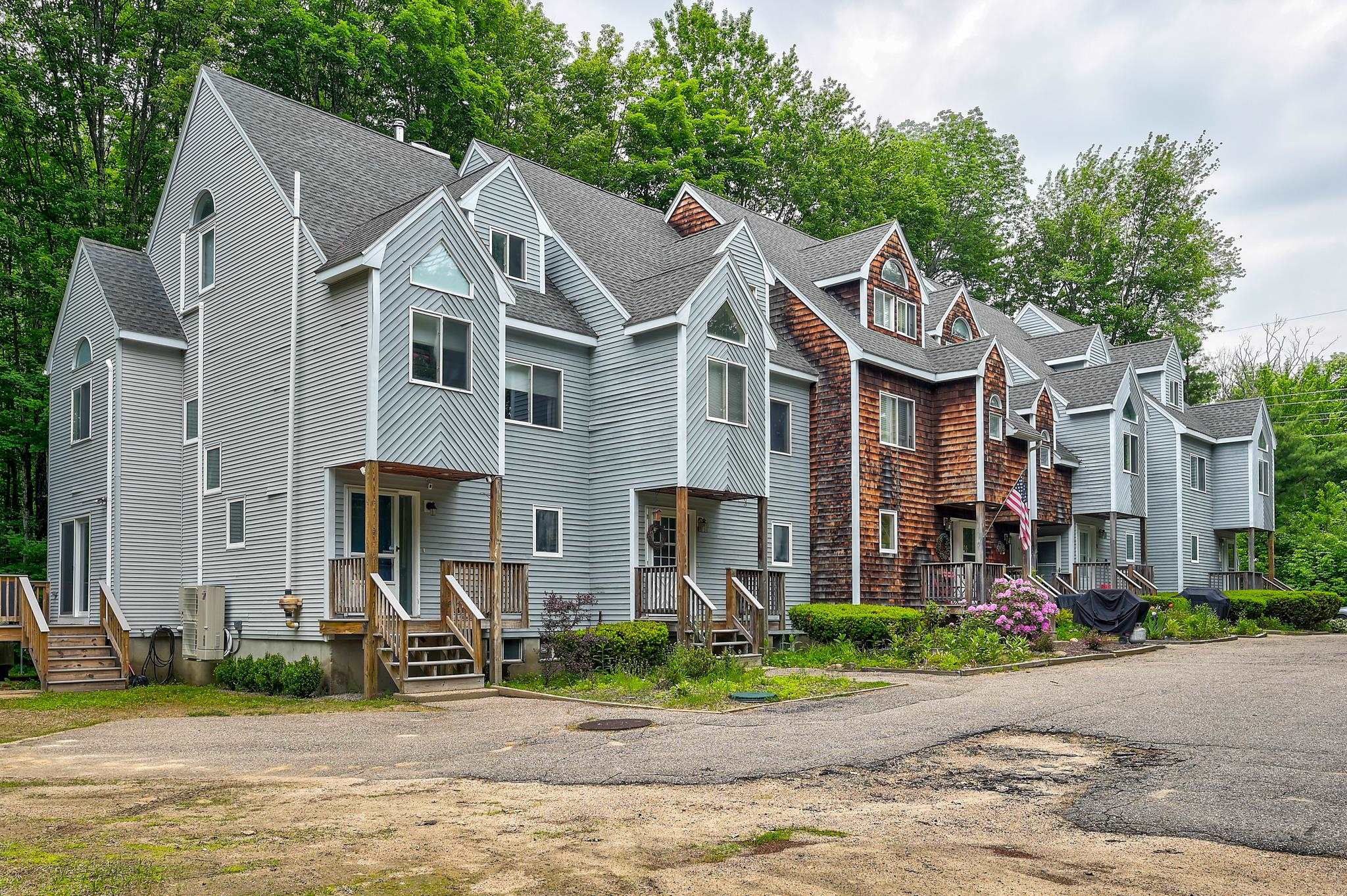 Row of gray condominiums with gabled roofs, wooden porches, and a shingled central section.