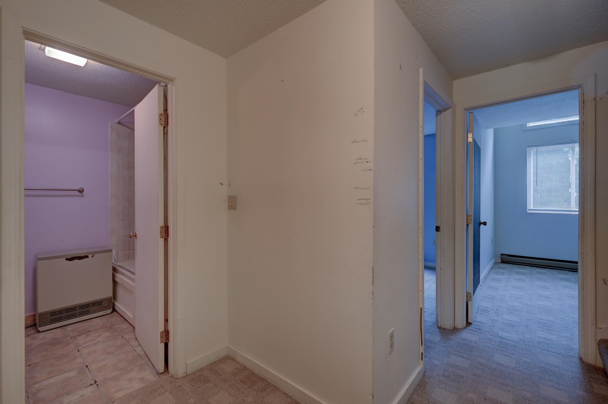 Vacant hallway with open doorways to a tiled bathroom and an empty carpeted room.