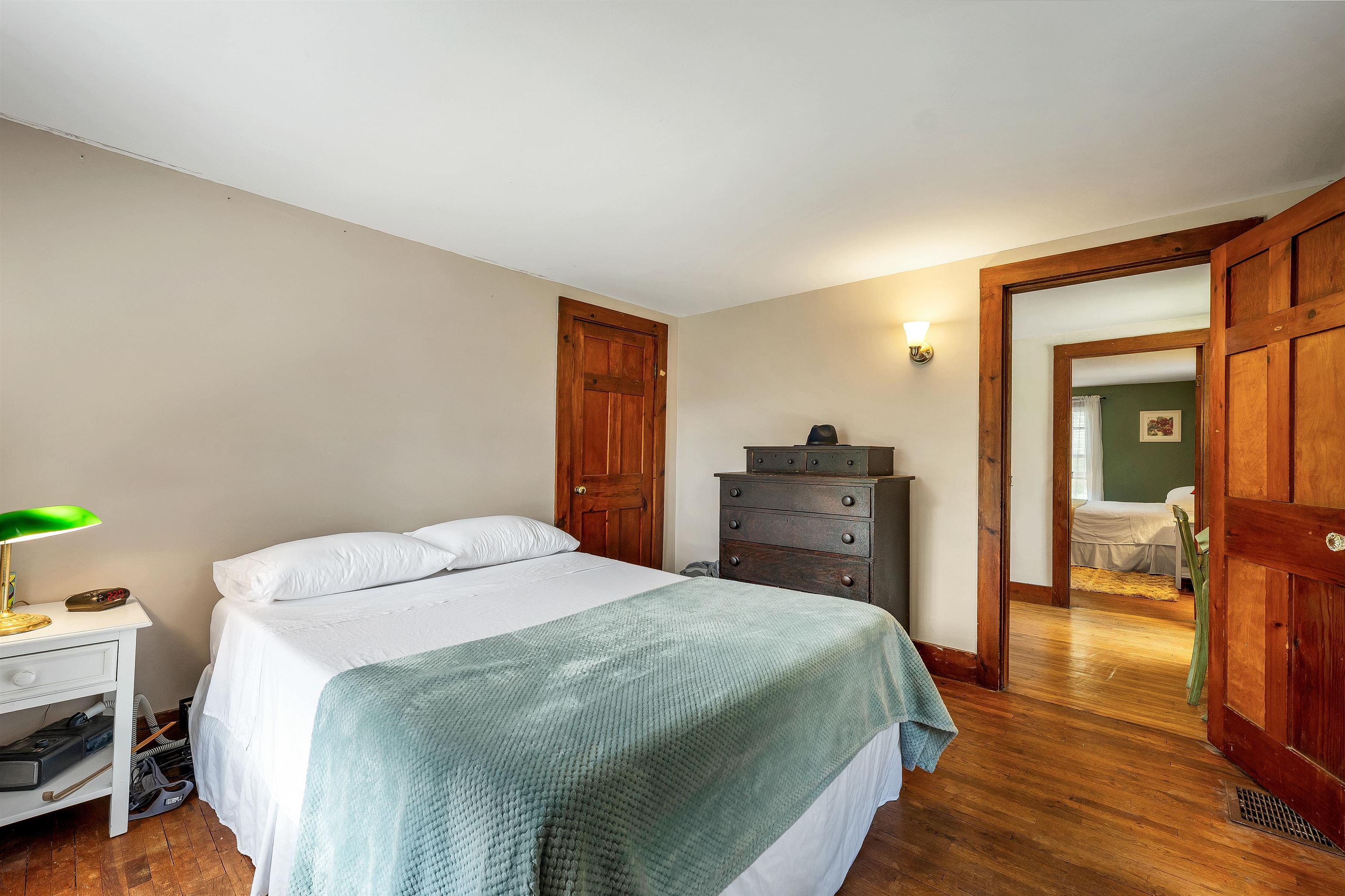 Bedroom with a pale blue-green bed coverlet, dark dresser, and wood-trimmed doorway to another room.