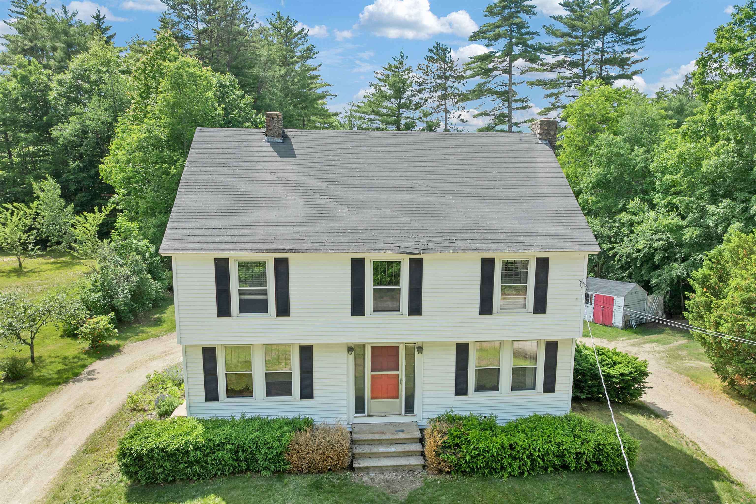 White two-story house with black shutters, a steep gray roof, and a red front door