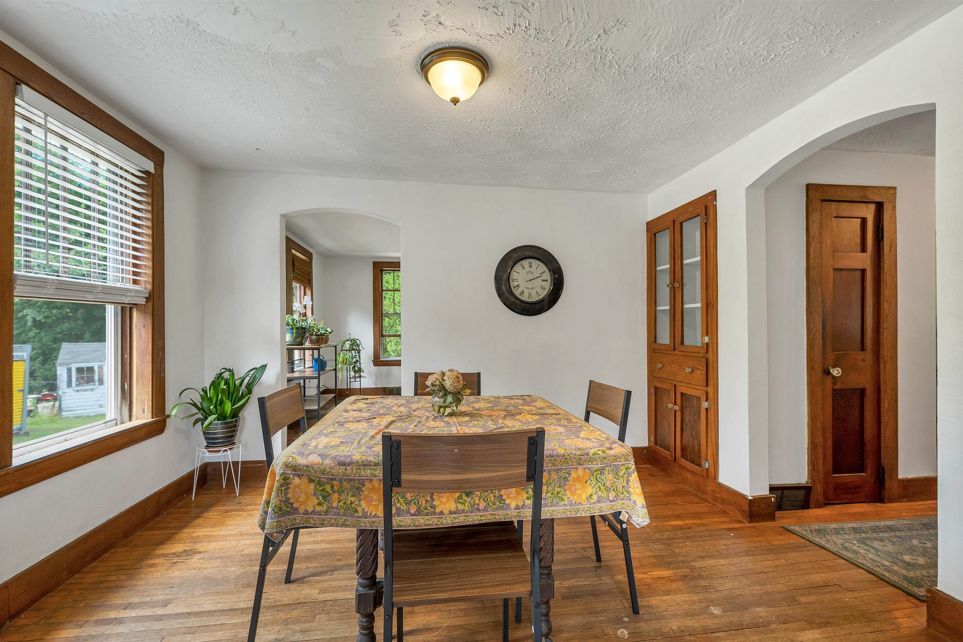 Dining room with a floral-covered table, hardwood floors, and wood-trimmed windows.