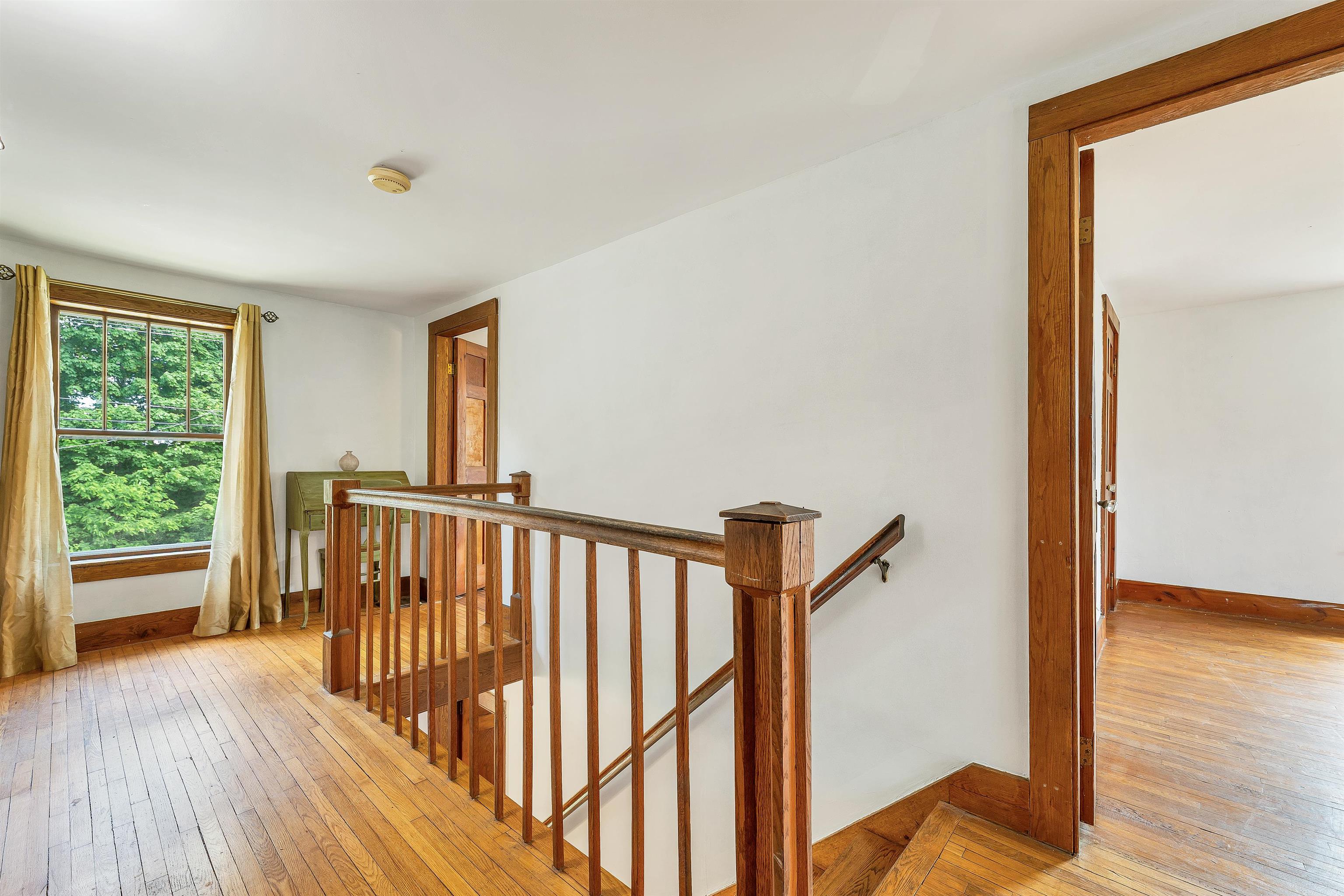 Upstairs landing with hardwood floors, a wooden stair railing, and a large curtained window.